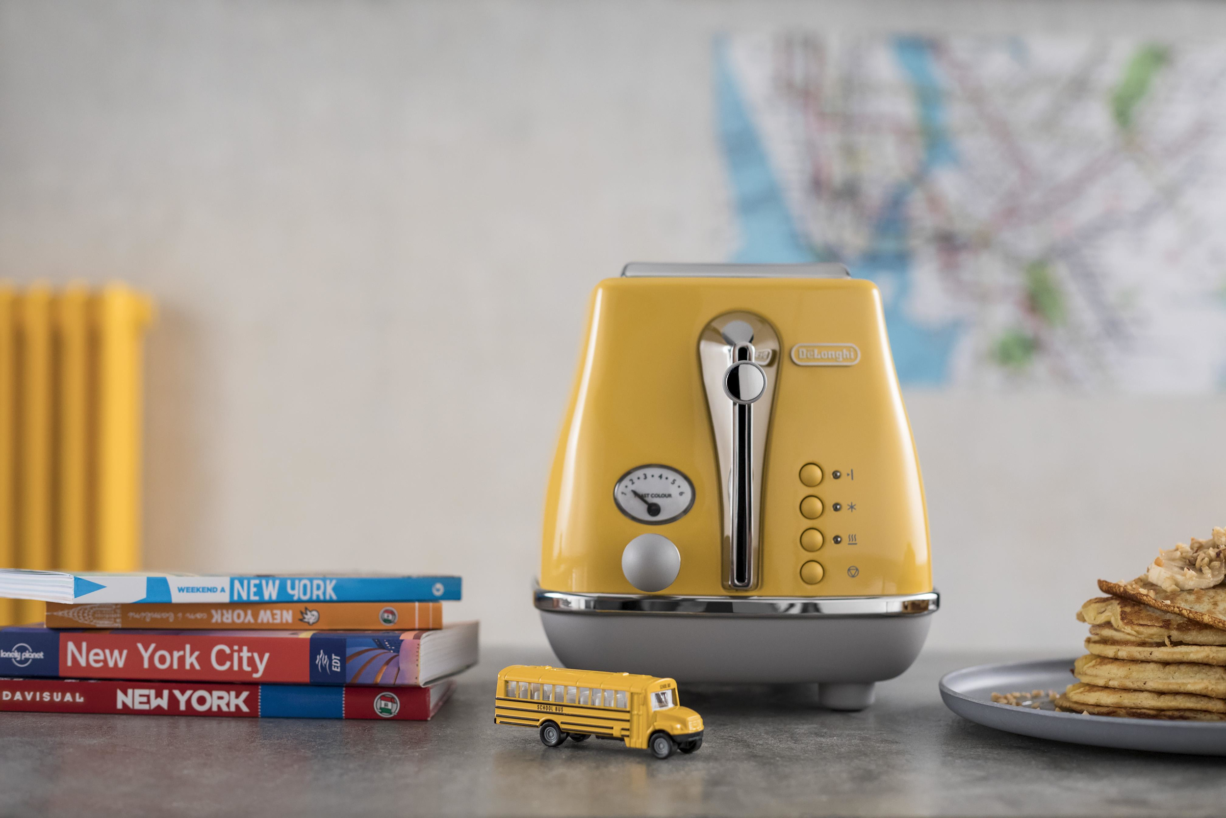 Żółty toster, książki, zabawkowy autobus i naleśniki na stole.