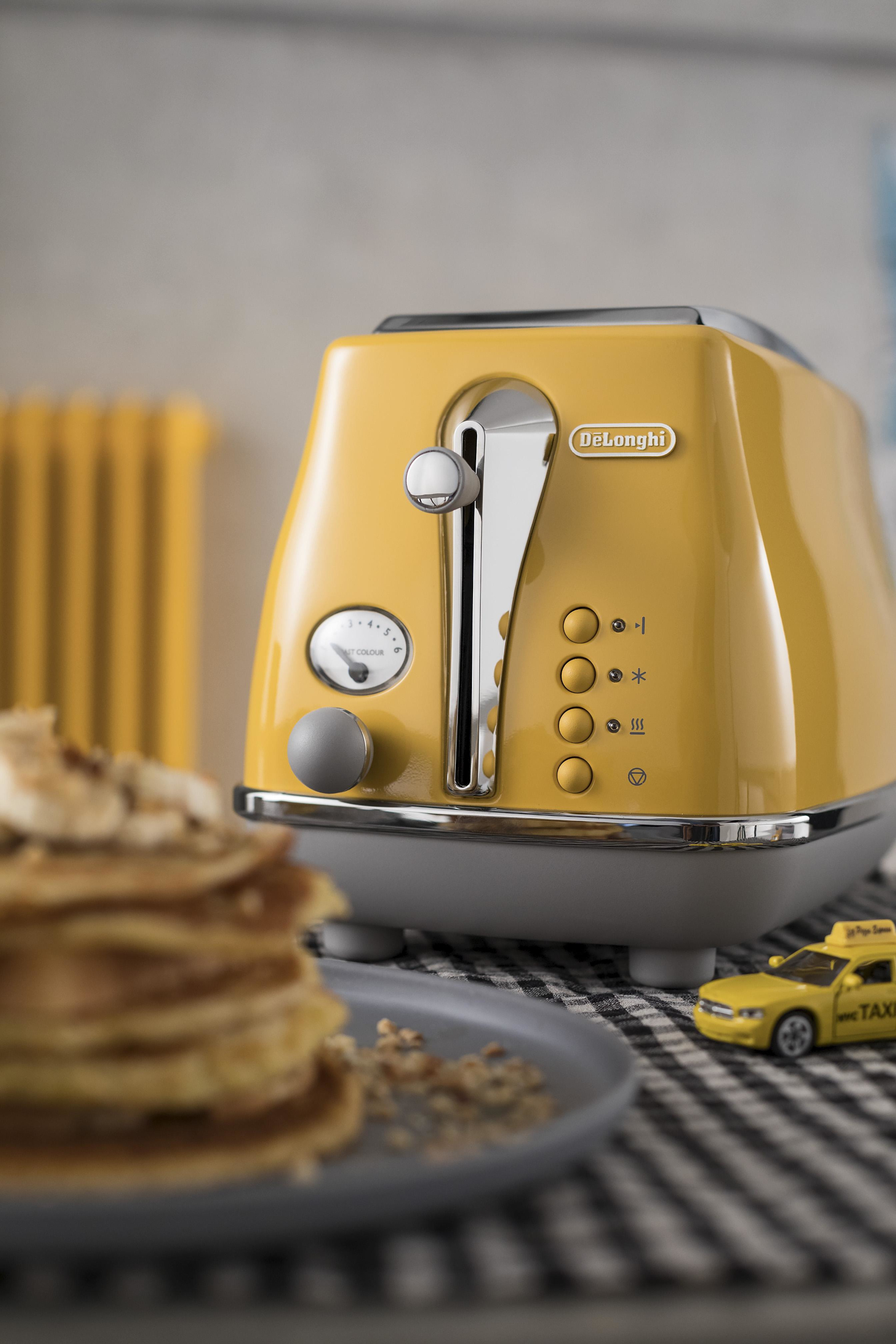 Żółty toster z naleśnikami i zabawką taksówką na kraciastej serwetce.