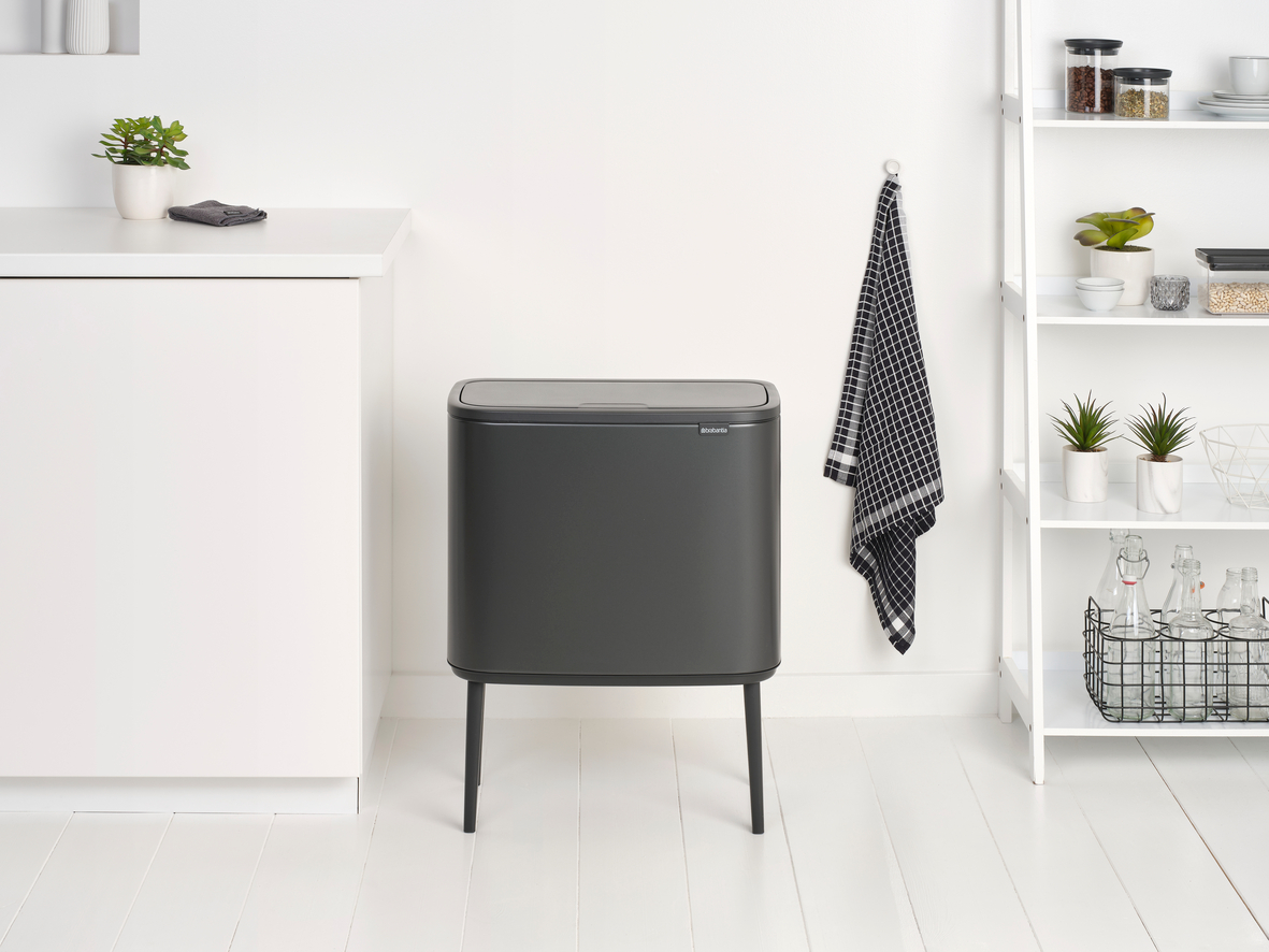 Moderner grauer Mülleimer auf schwarzen Beinen in einer weiß getäfelten Küche.