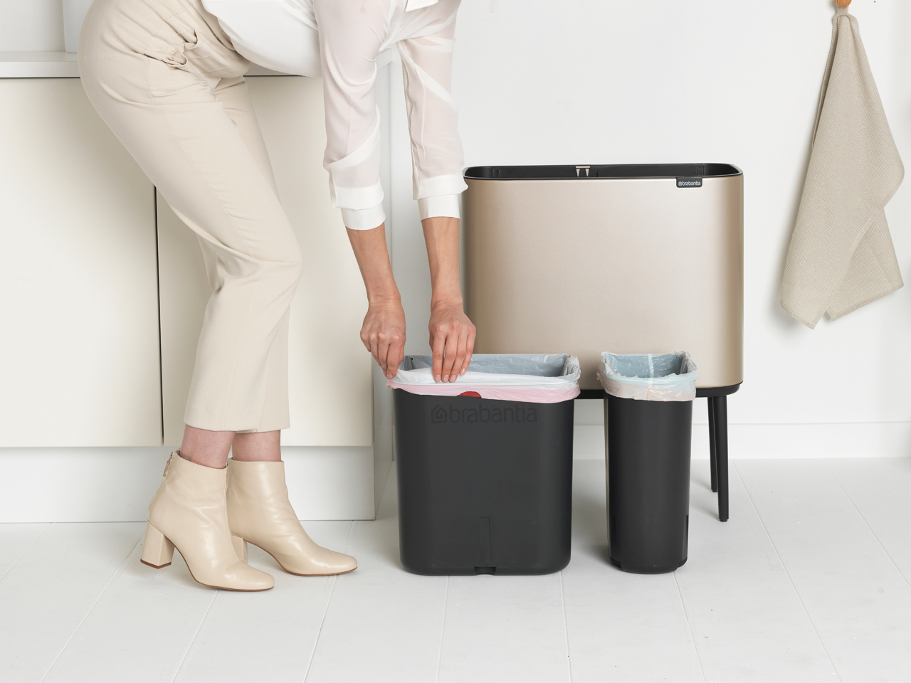 Frau in der Nähe von schwarzen Mülltonnen, die einen Beutel in eine legt. Beige Wand und Boden.