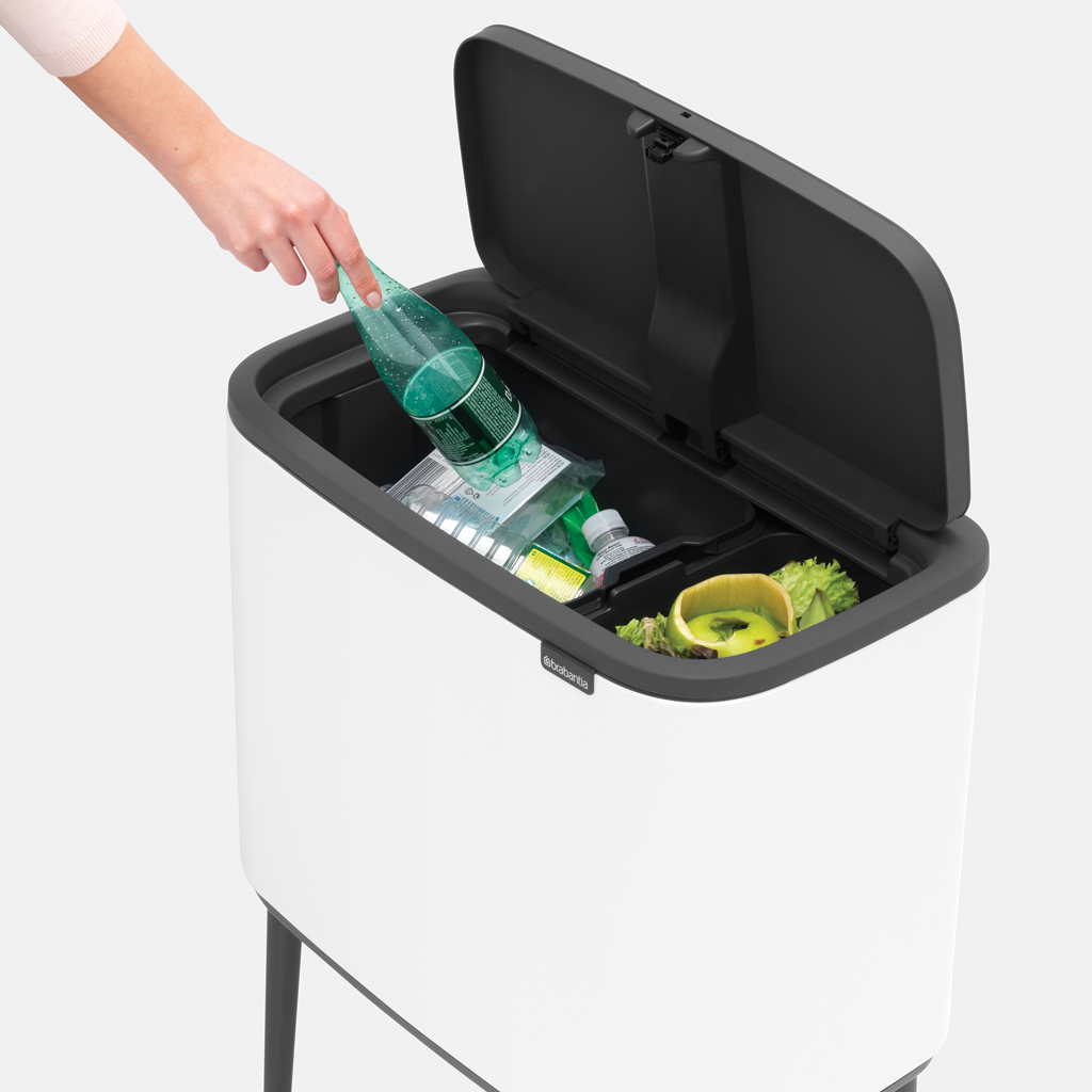 Person legt grüne Flasche in weiß-schwarze Mülltonne. Tonne hat zwei Bereiche.