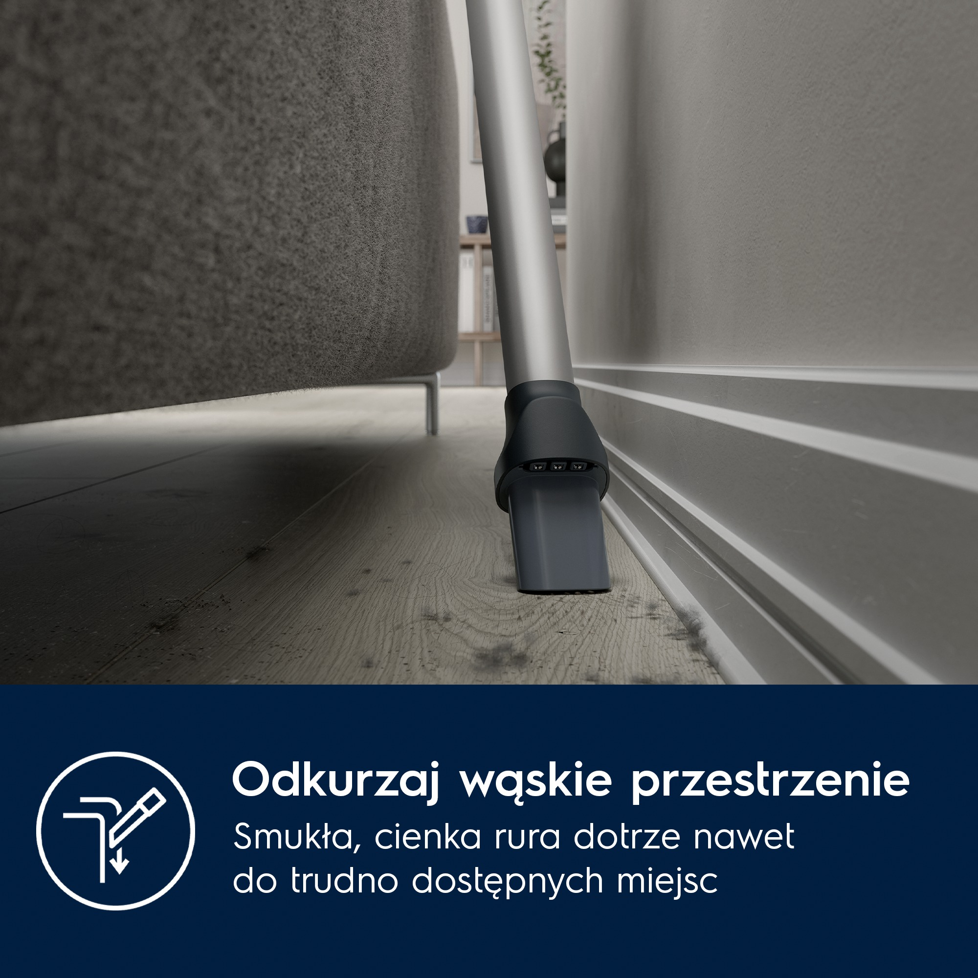 Rura odkurzacza czyści wąską szczelinę między sofą a ścianą.
