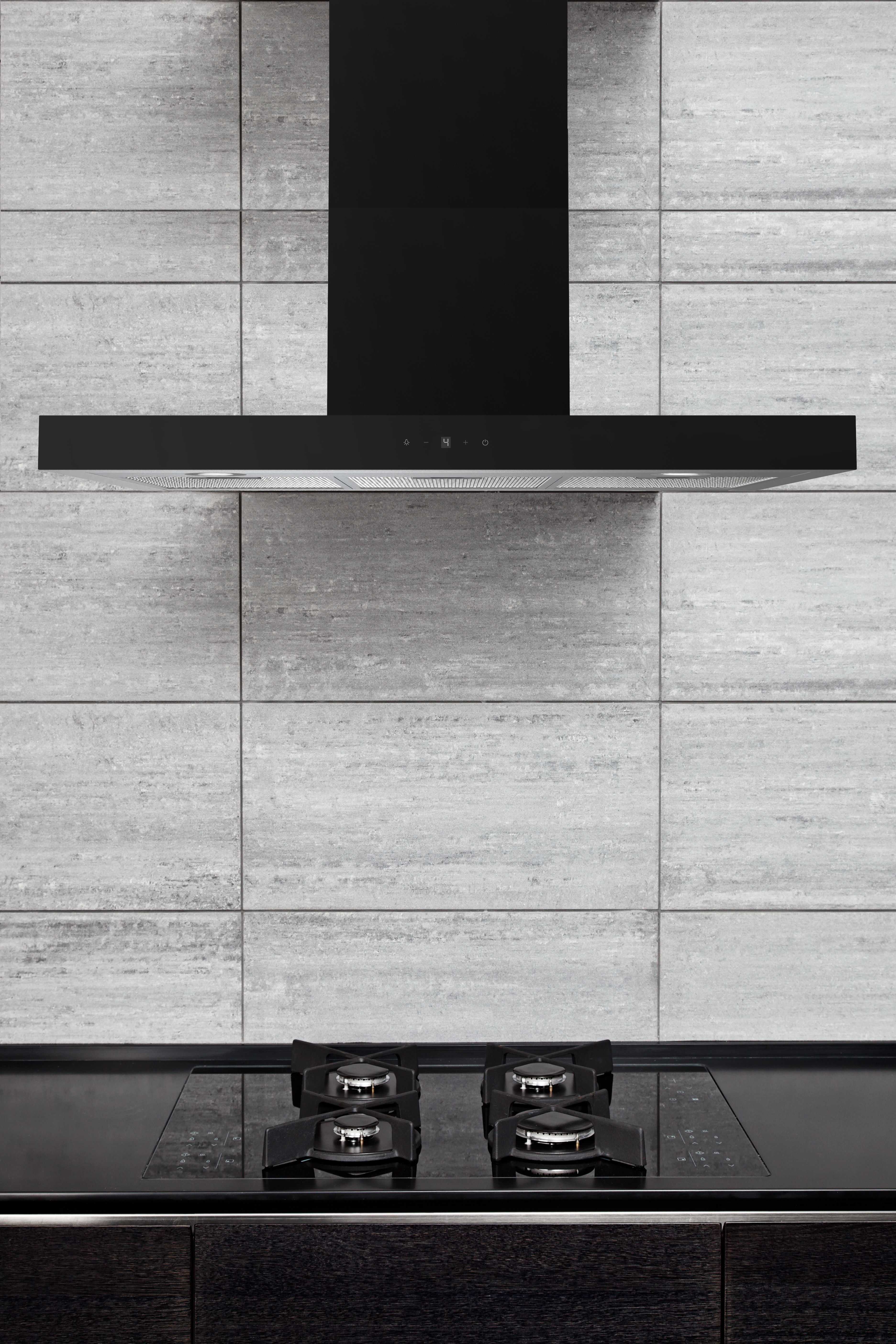 Black range hood above a black glass cooktop on a gray tiled wall.