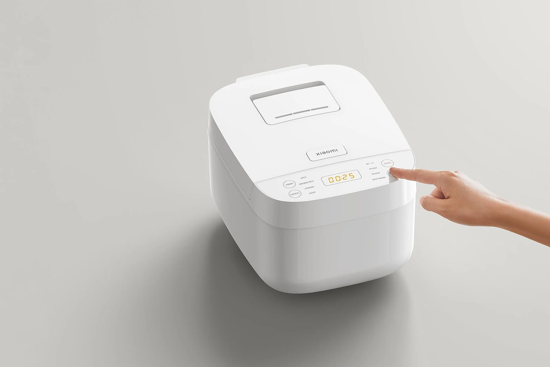 Fehér Xiaomi rizsfőző, egy ujj gombot nyom.