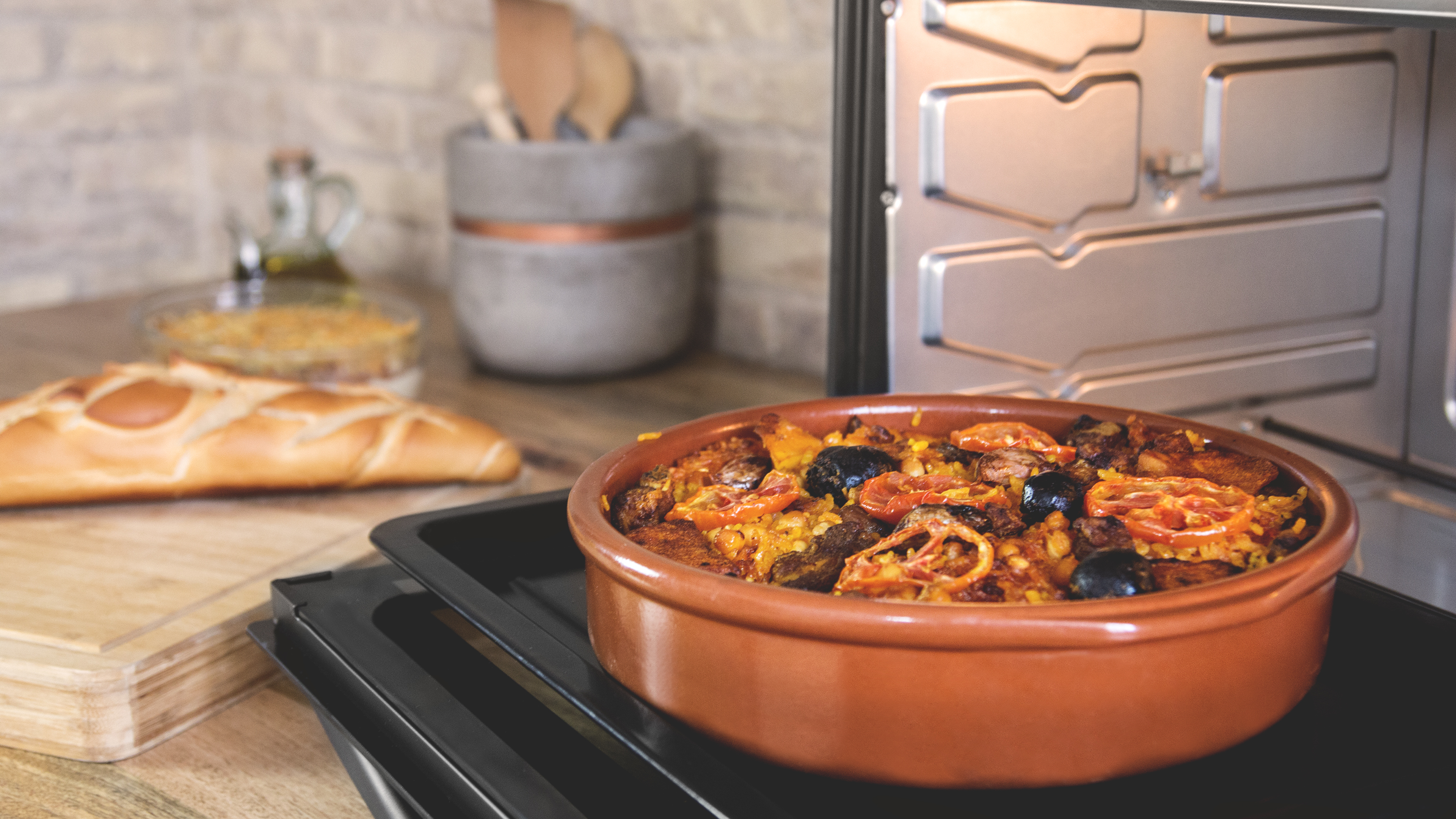Plato con comida en un horno. Contiene un plato marrón con comida, cerca de utensilios de madera.