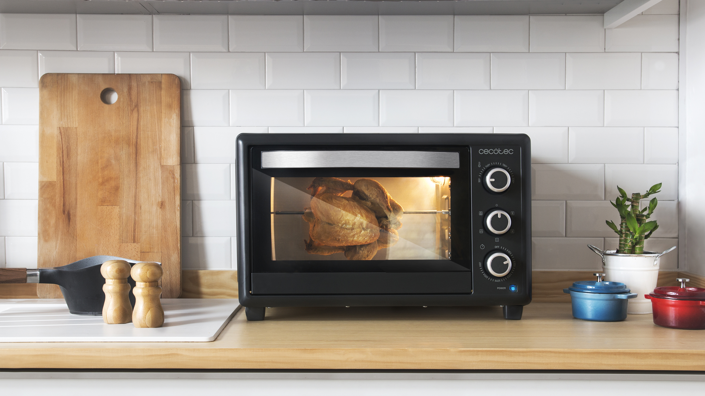 Un horno negro con pollo asado, una tabla de madera y ollas pequeñas sobre una encimera.