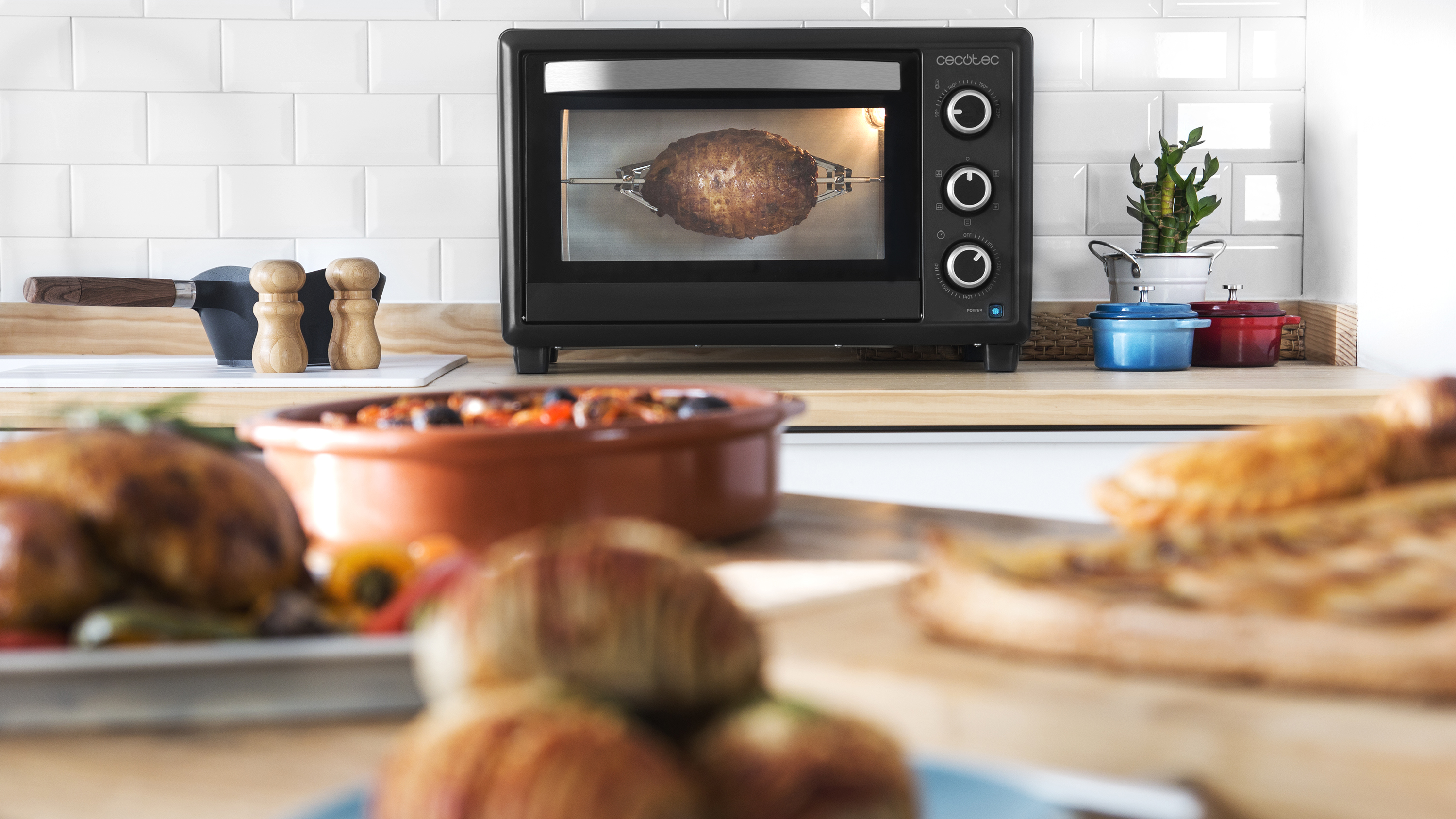 Un horno negro con comida adentro sobre una encimera de cocina. Otra comida en primer plano.