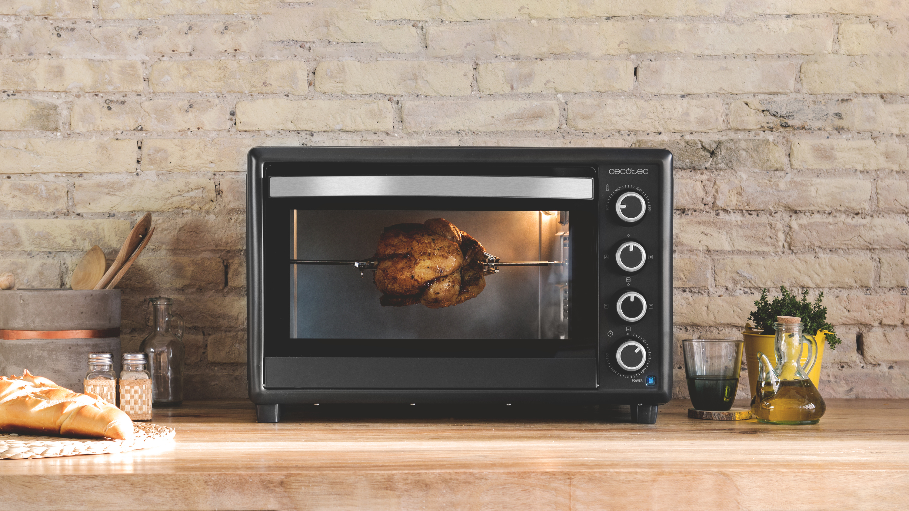 Horno negro con un pollo asado dentro. El horno está sobre una encimera de madera con comida y utensilios.