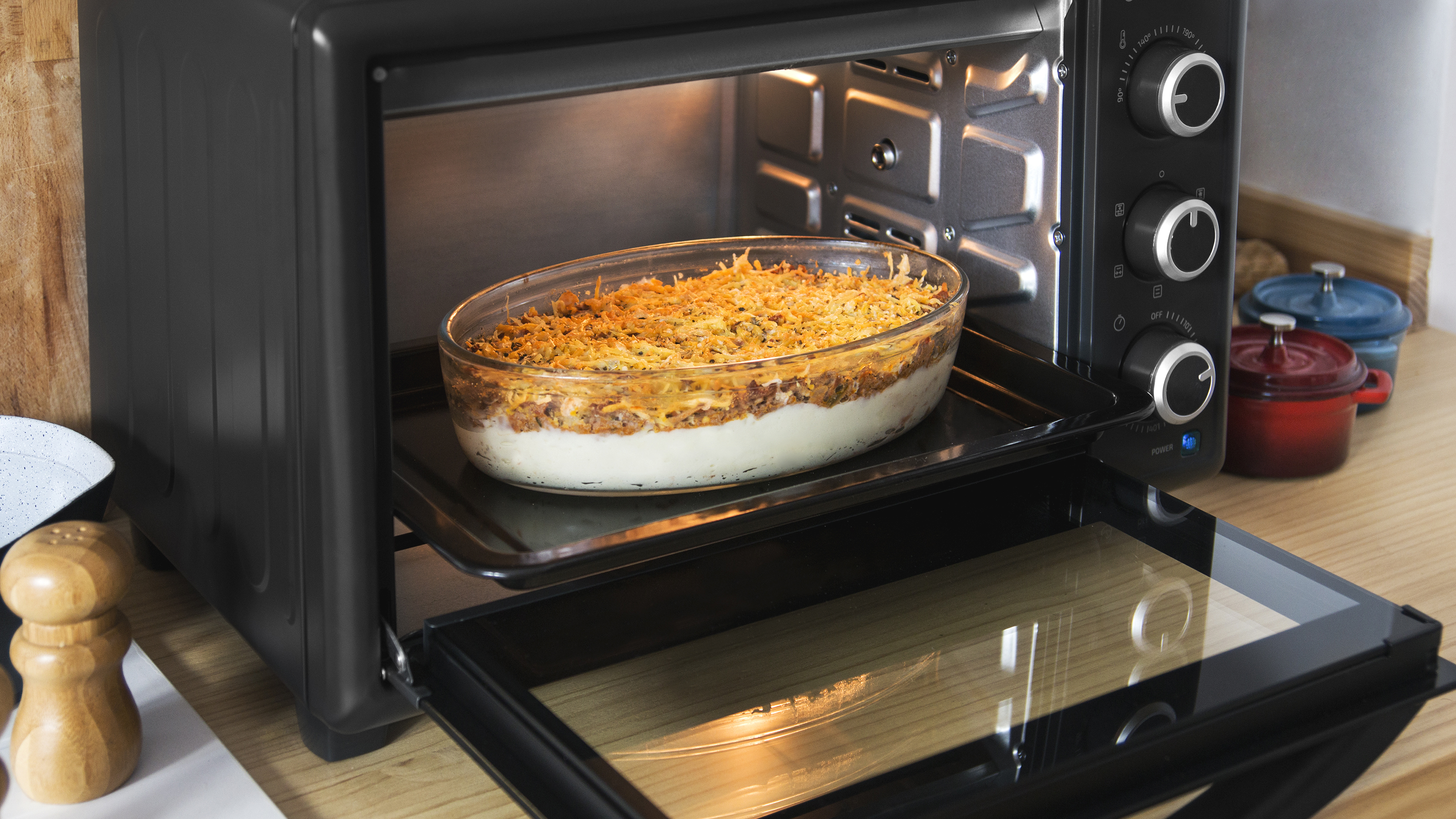 Horno con puerta abierta. Cazuela en plato de vidrio sobre una bandeja. Interior iluminado.
