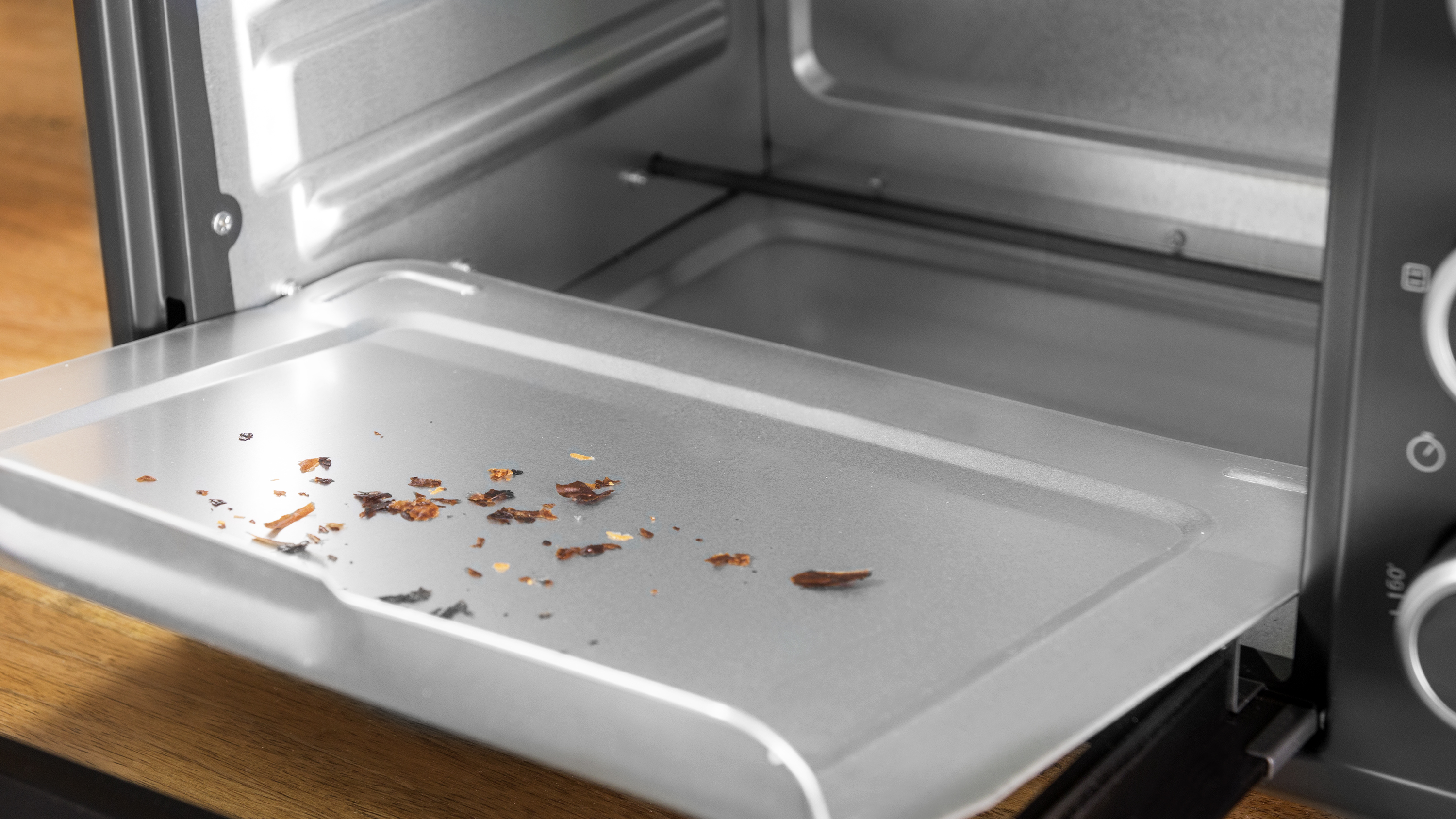 Horno tostador abierto con bandeja, algunas migas en la bandeja.