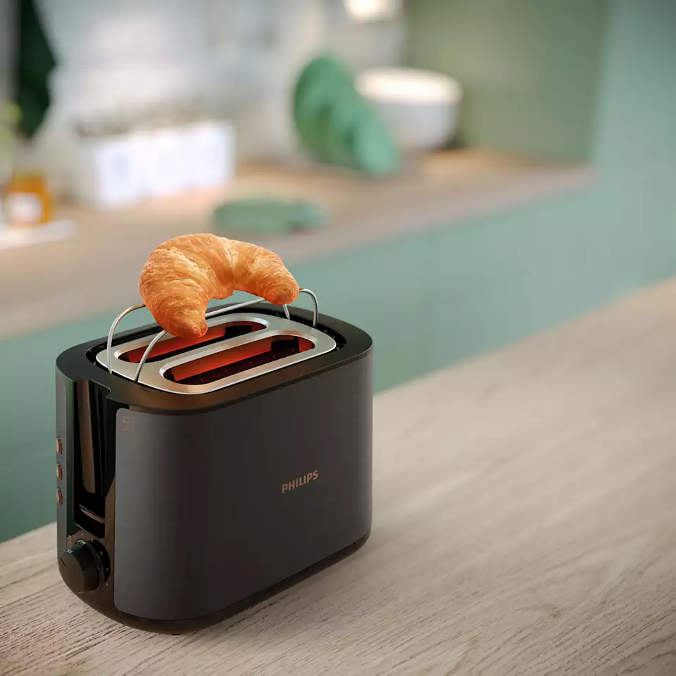 Egy fekete kenyérpirító egy croissant-val a tetején, fa felületen. Zöld háttér.