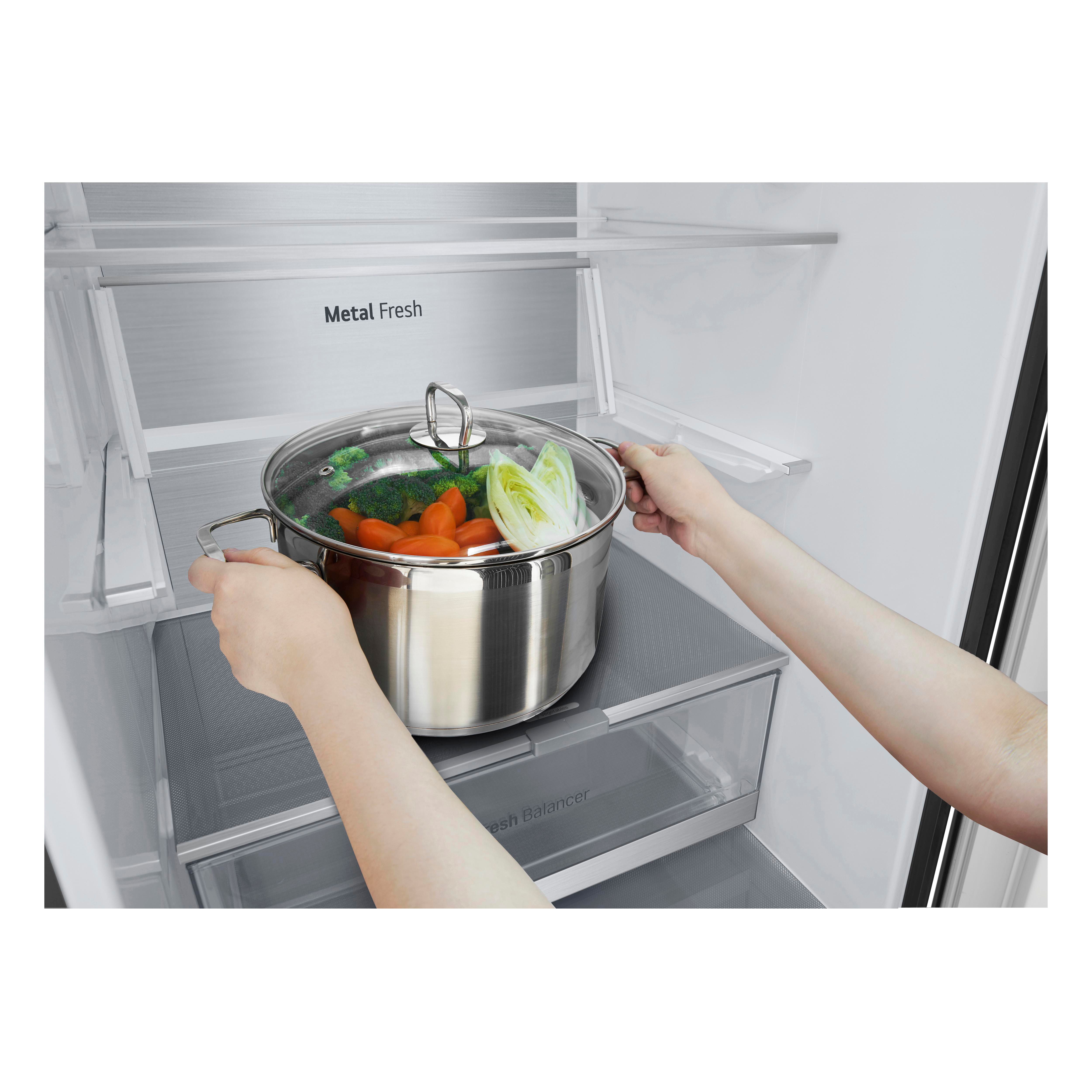 Hände halten einen Topf mit Gemüse in einem Kühlschrank.