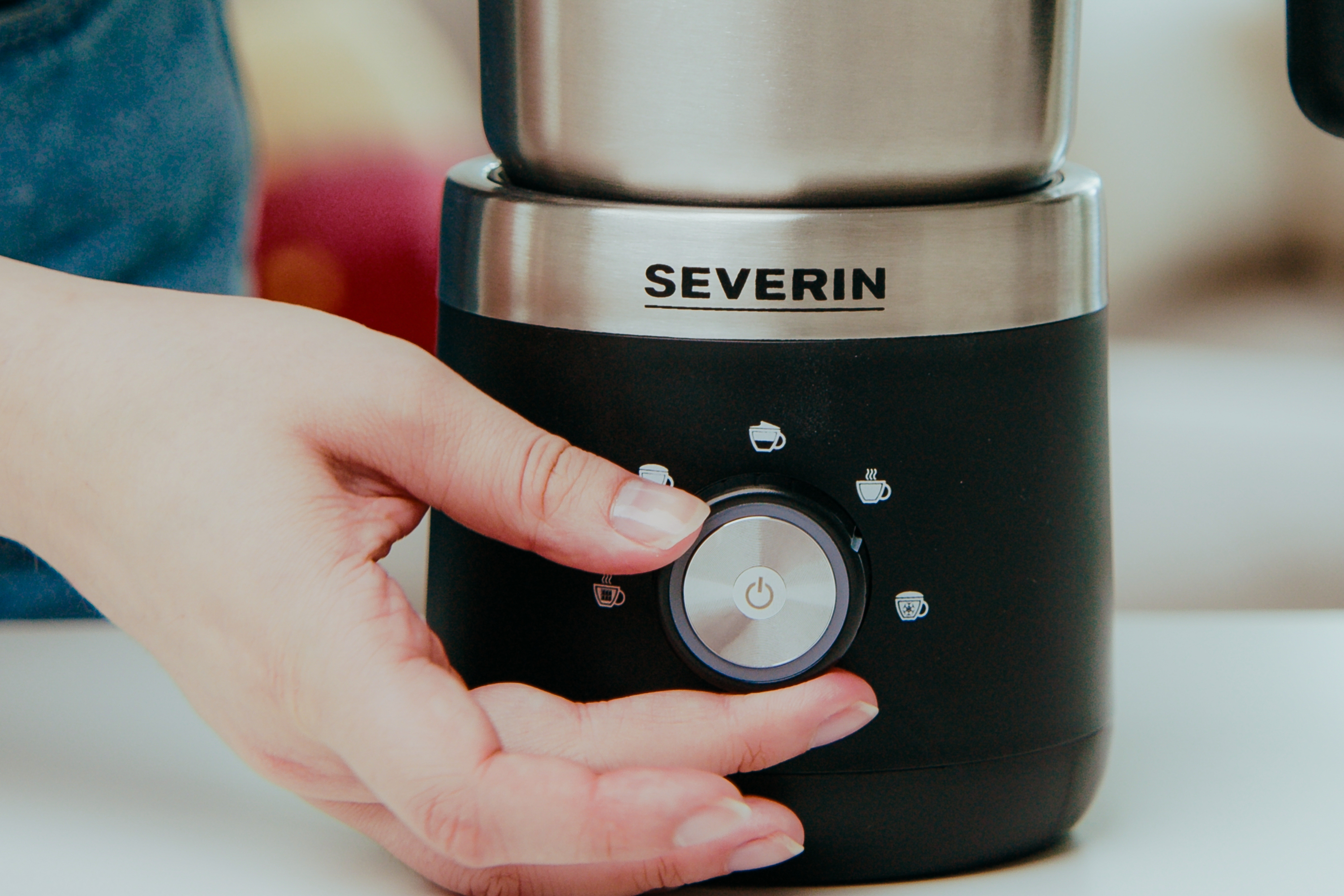 Die Hand einer Person, die einen Drehregler an einer schwarz-silbernen Kaffeemaschine dreht.