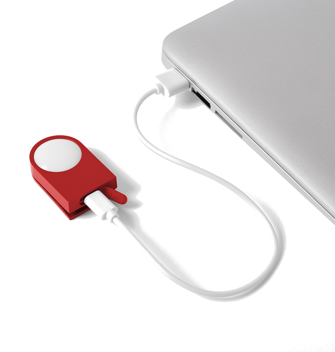 Czerwony gadżet z białą górą jest połączony z laptopem białym kablem. Laptop jest srebrny. Tło jest białe.