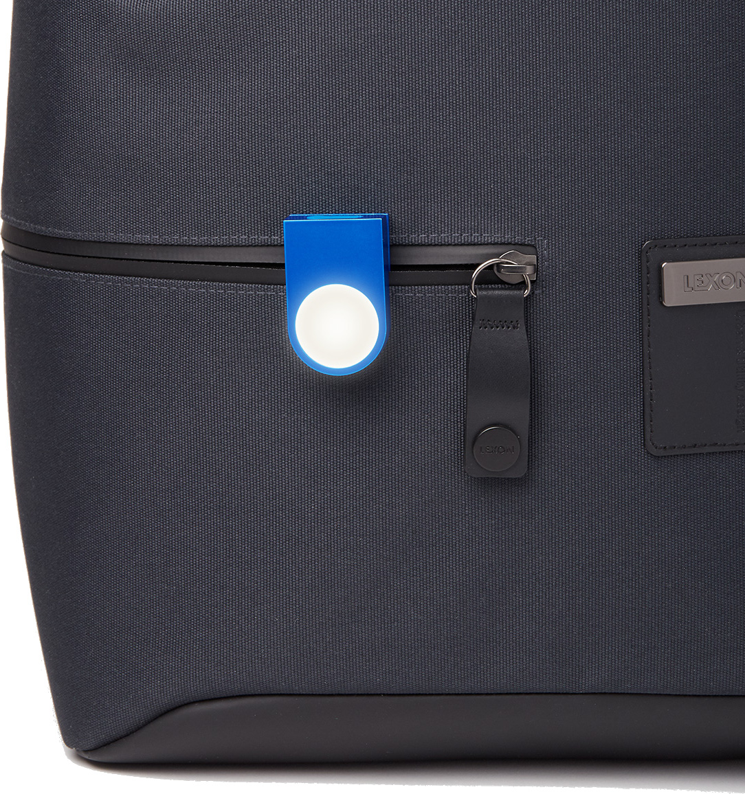 Zbliżenie ciemnoszarego plecaka z niebieską lampką na klips i czarnym zamkiem błyskawicznym. Światło ma białe, okrągłe centrum.