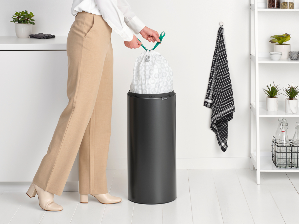 Eine Frau in einer Küche zieht einen Müllbeutel aus einem dunkelgrauen Brabantia-Mülleimer.