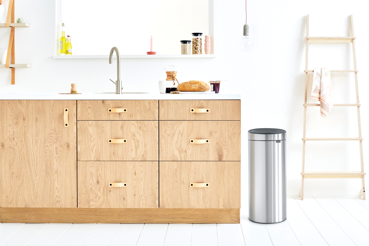 Eine moderne Küche mit Holzschränken, einem Waschbecken und einem Mülleimer aus Edelstahl.