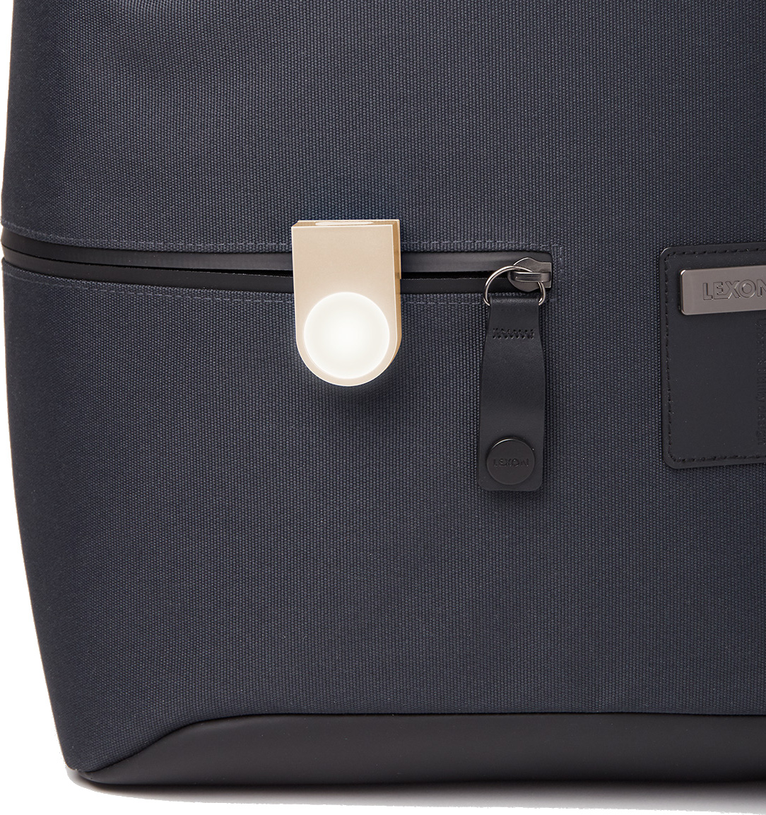 Czarna torba pokazuje beżowe okrągłe urządzenie przymocowane do zamka błyskawicznego i małą metalową metkę.