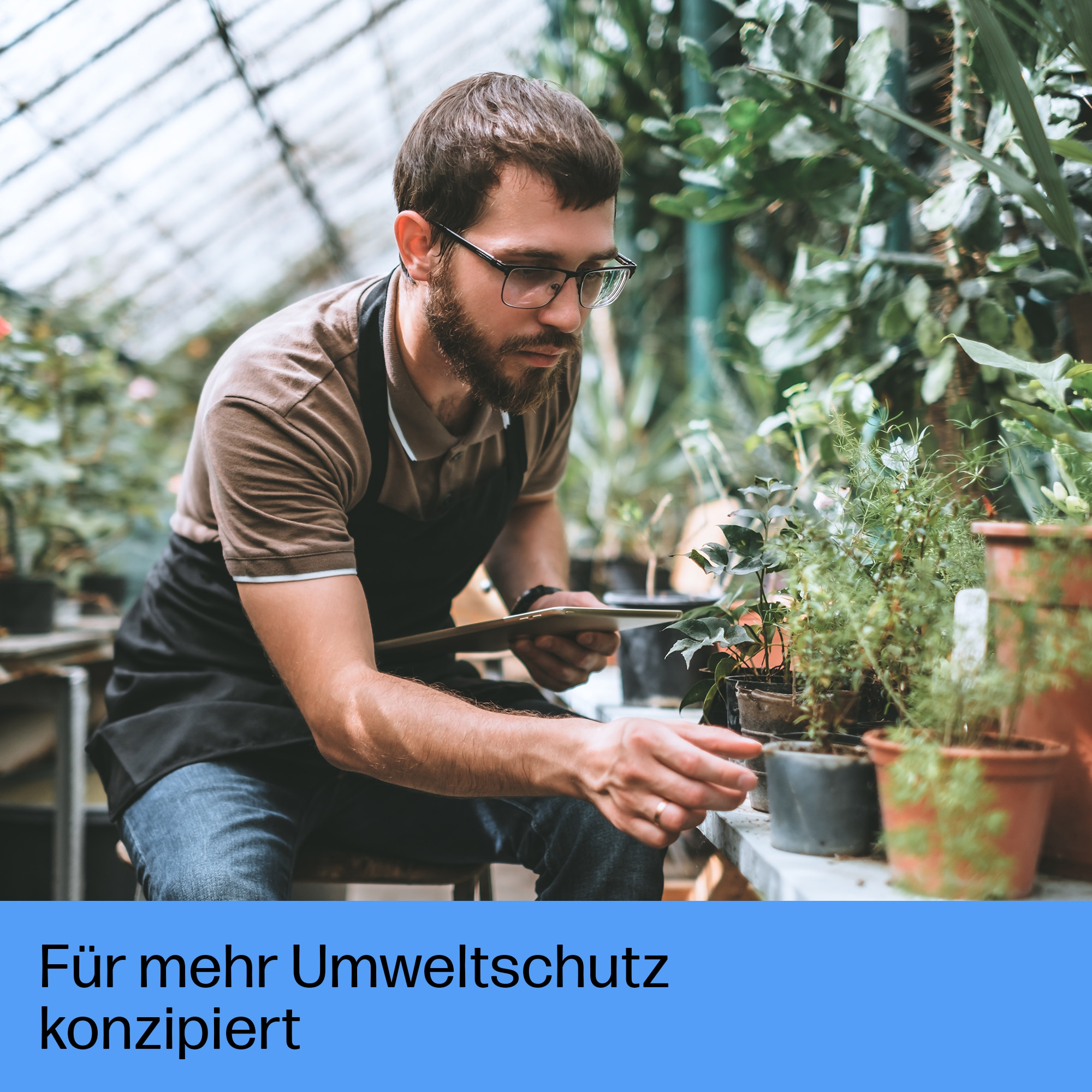 Un jardinier avec des lunettes et un tablier s'occupe de plantes en pot dans une serre.