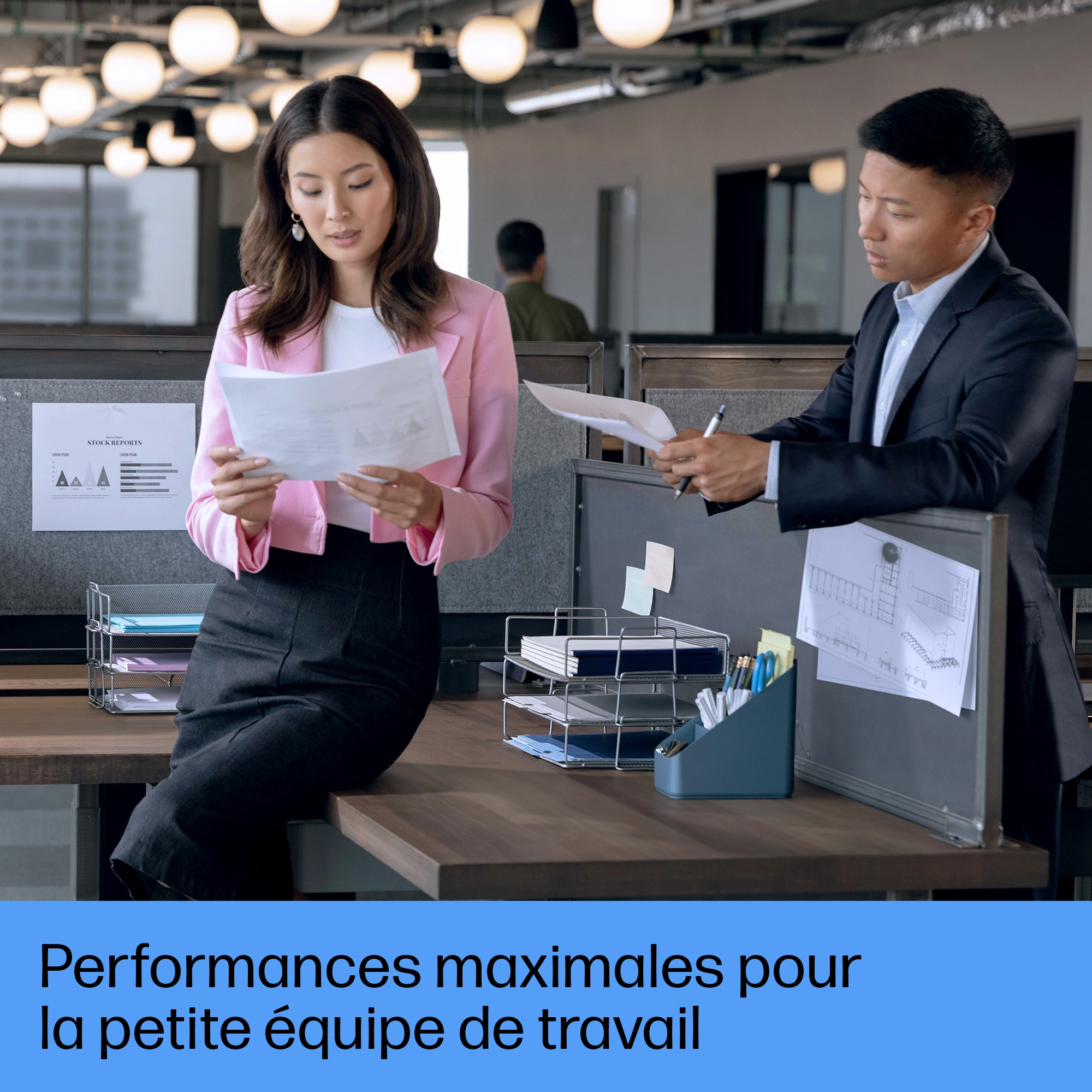 Une femme en rose et un homme en costume examinent des documents dans un bureau.