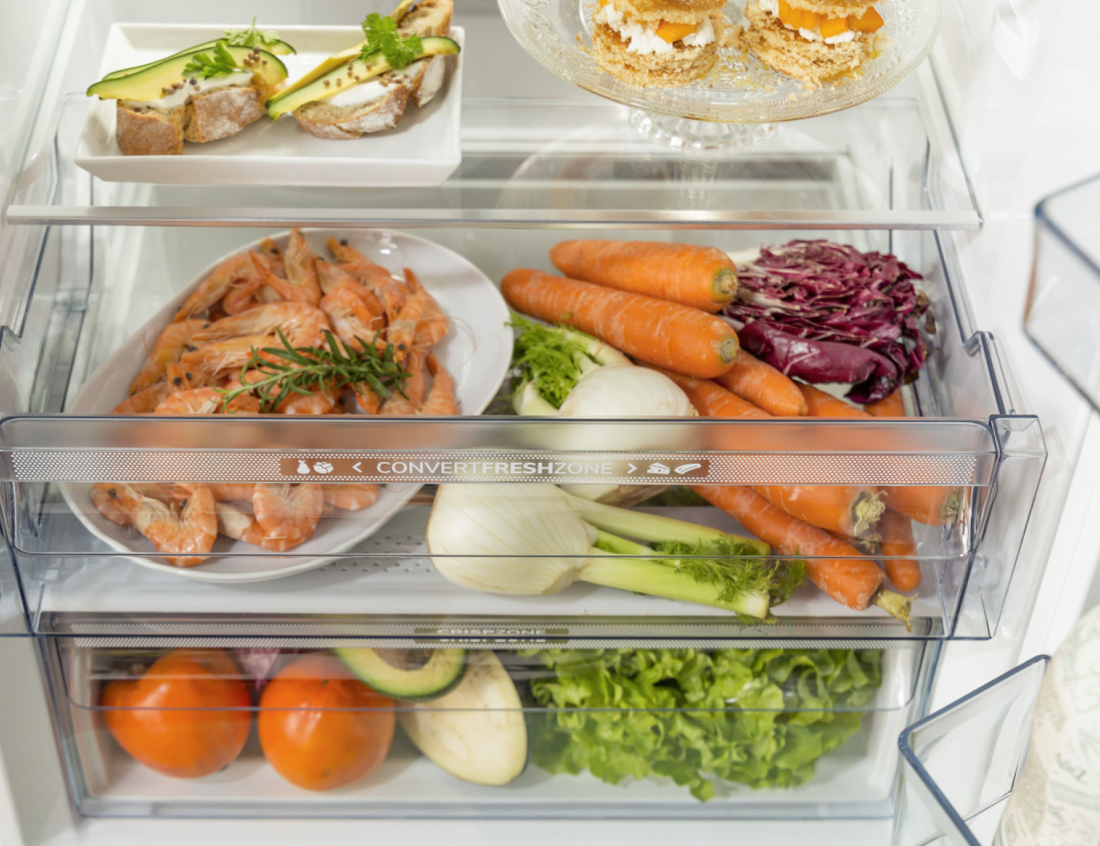 Otwarta lodówka z jedzeniem. Krewetki, marchew i warzywa w przezroczystych szufladach.