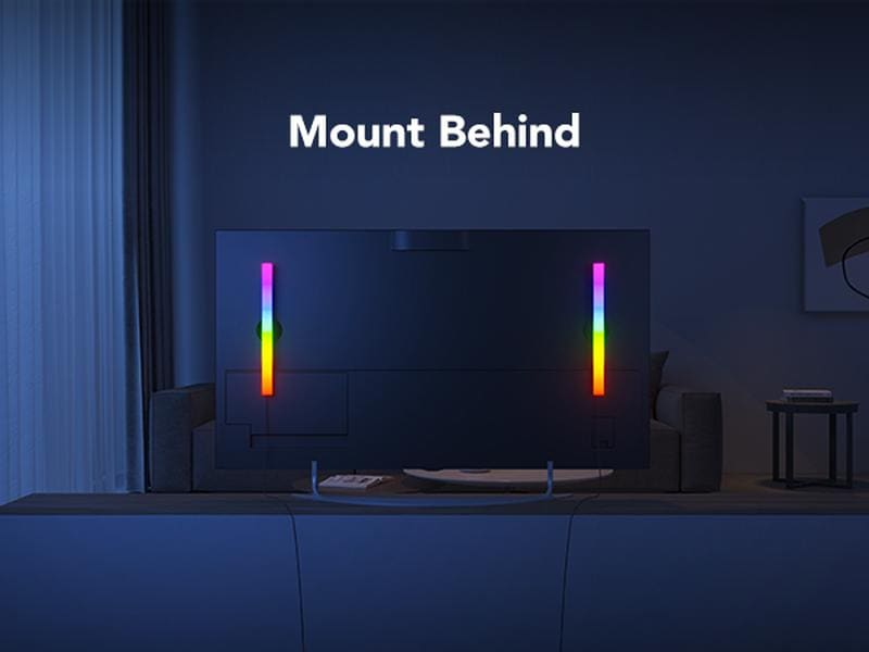 Fernseher mit bunten Lichtern an den Seiten, dahinter montiert. Sofa und kleiner Tisch im Hintergrund. Die Wand ist dunkel.