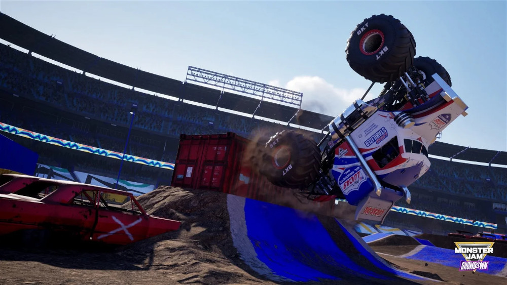 Un monster truck en l'air dans un stade avec une voiture renversée au premier plan.