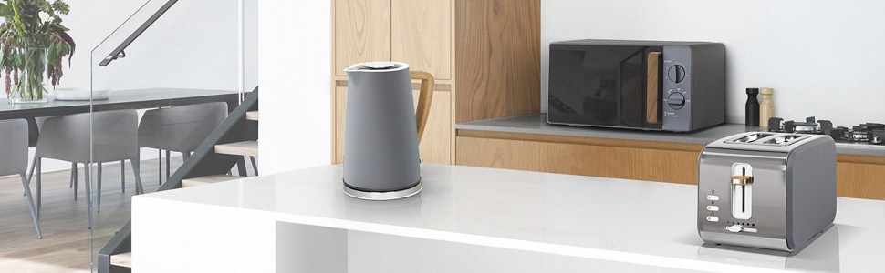 Scena cucina con bollitore grigio, microonde, tostapane e piano lavoro bianco.