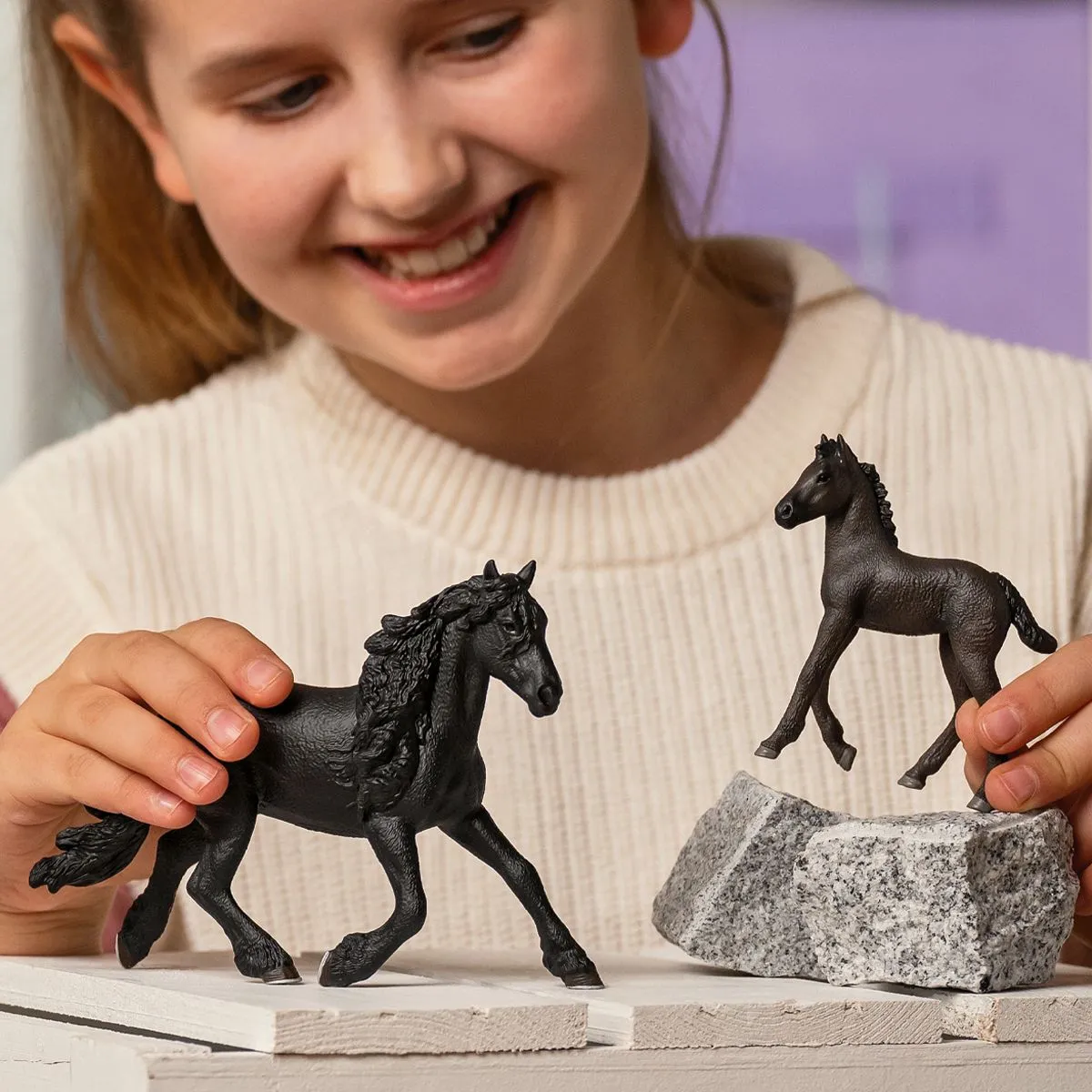 Ein Mädchen hält schwarze Spielzeugpferde, eines steht auf einem Felsen.