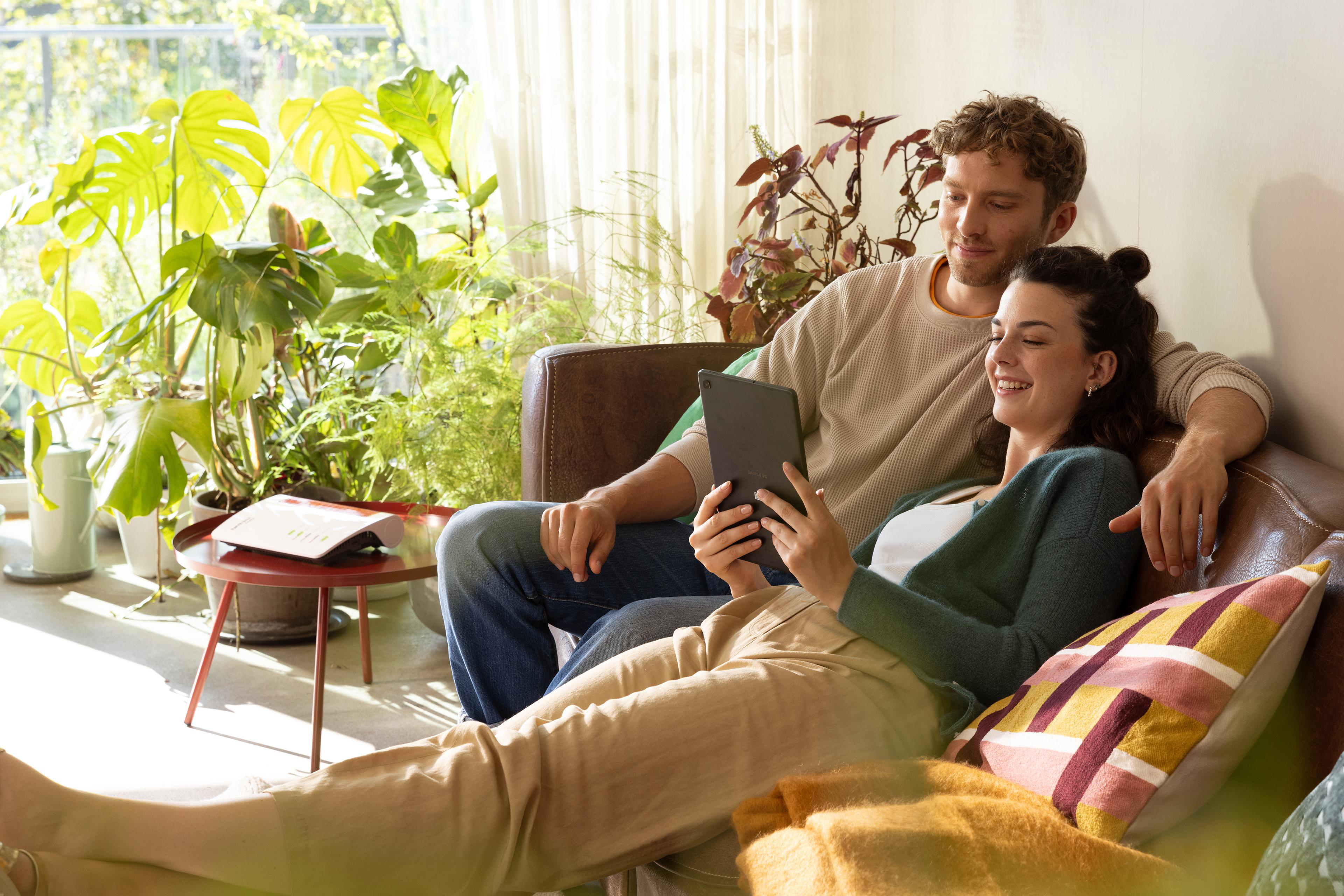Ein Paar auf einem Sofa, die Frau schaut auf ein Tablet, in einem Wohnzimmer.