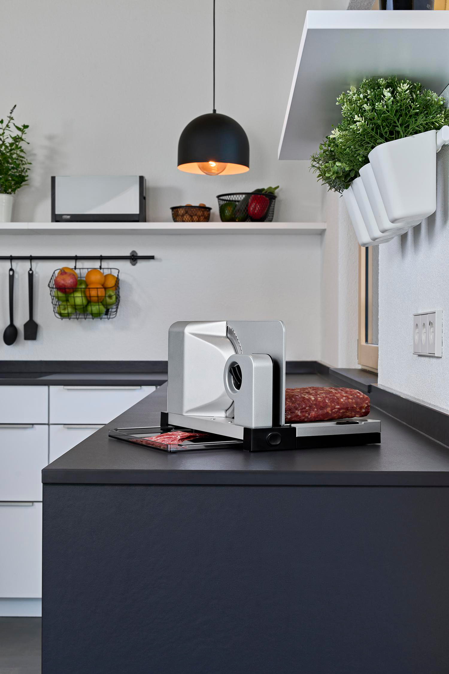 Eine Küchenszene mit einer Fleischschneidemaschine, Essen und verschiedenen Küchenutensilien.