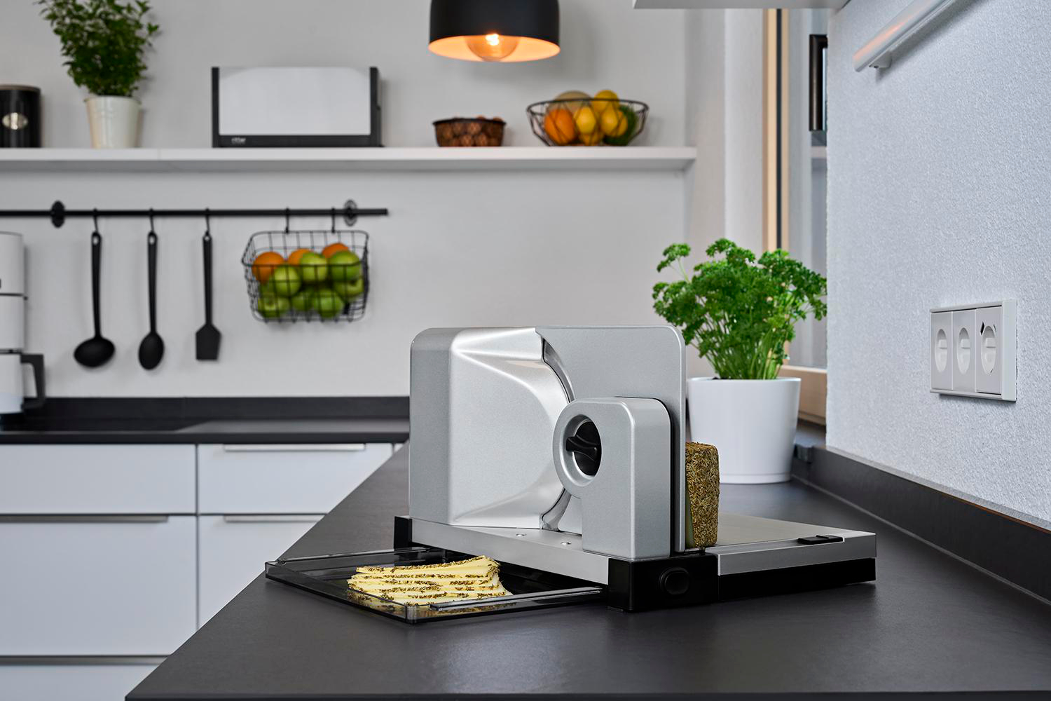 Eine Küchenszene mit einem Slicer auf einer Arbeitsplatte, schwarze Arbeitsplatte und weiße Wand.
