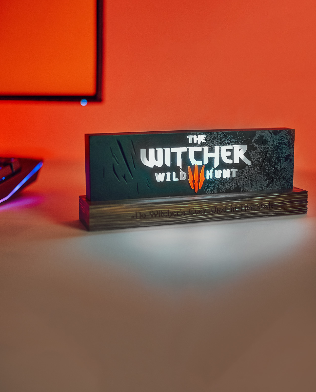 Ein beleuchtetes Witcher-Spielschild. Es steht auf einem Holzständer. Der Hintergrund ist orange und weiß.
