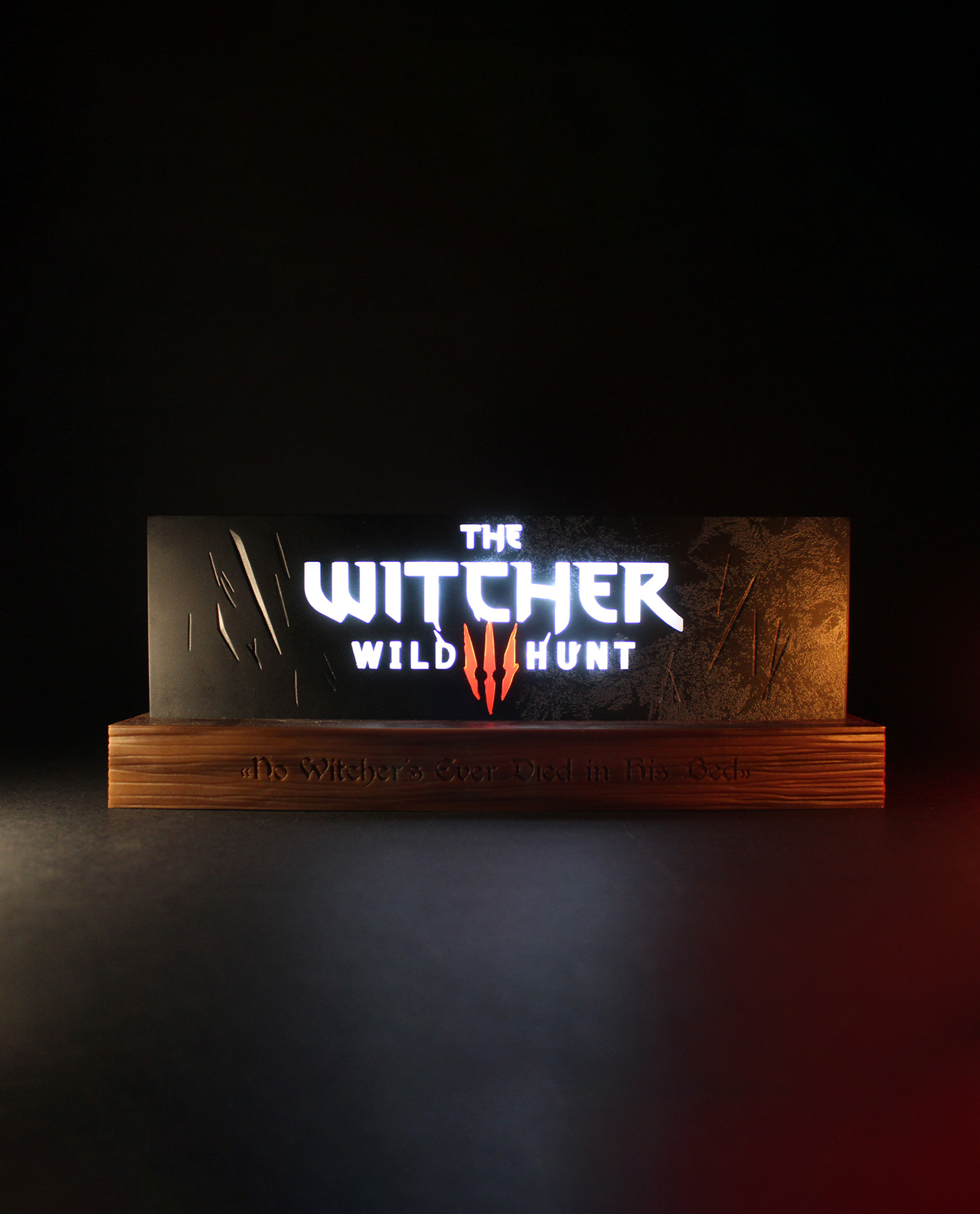 The Witcher Wild Hunt Display. Es hat einen Holzsockel und das Logo des Spiels. Der Hintergrund ist dunkel.