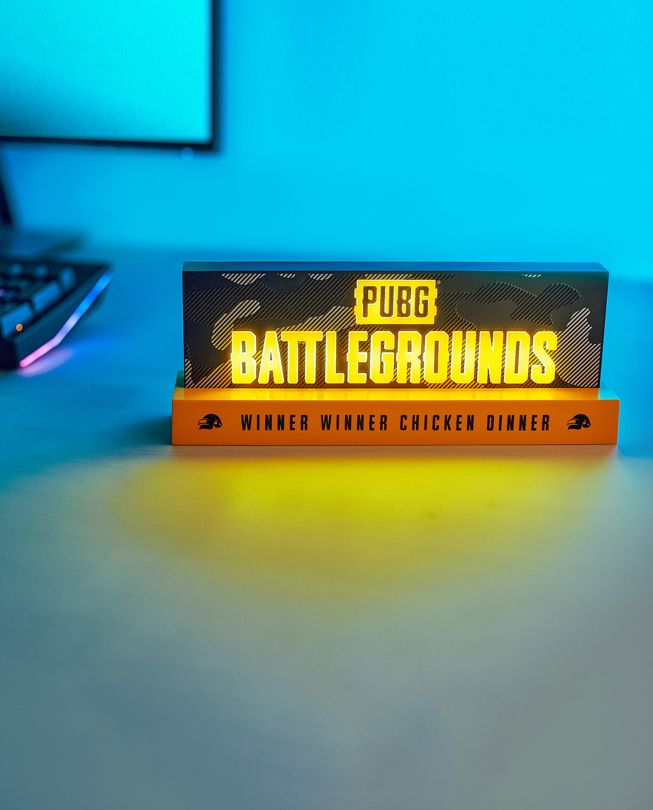 PUBG Battlegrounds Schild auf einem Schreibtisch, beleuchtet mit orangefarbenem und blauem Licht.