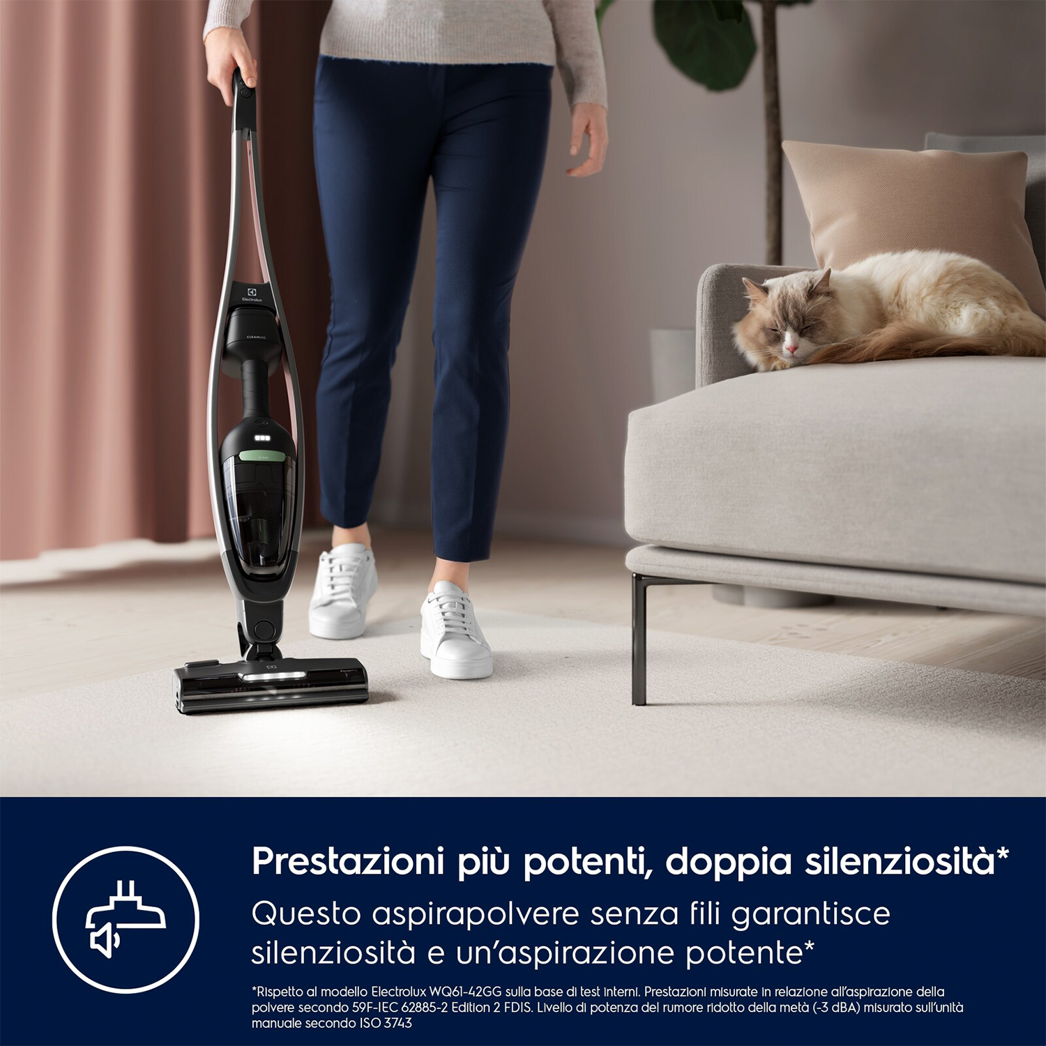 Una donna che aspira in un soggiorno con un aspirapolvere senza fili, gatto che dorme sul divano.