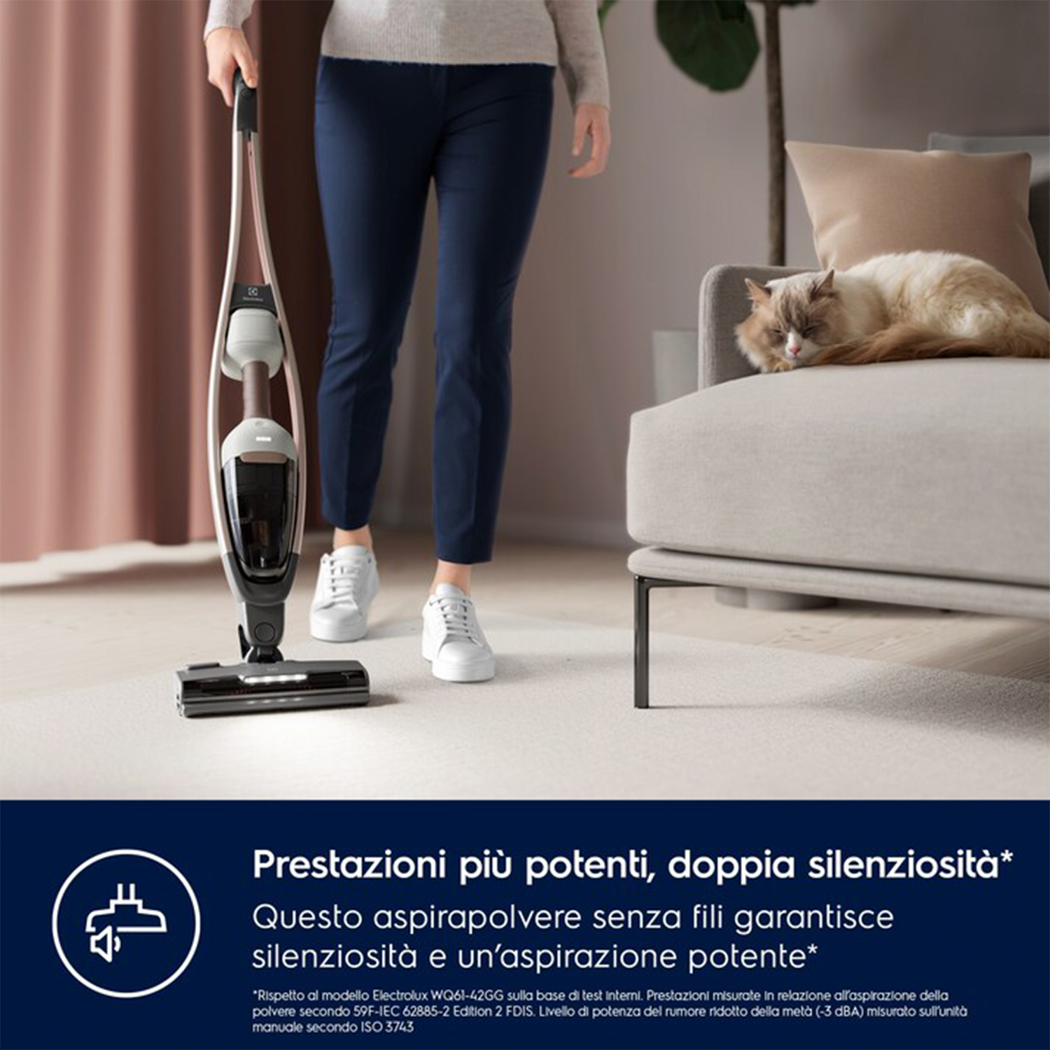 Una donna usa un aspirapolvere senza fili. Un gatto riposa su un divano.