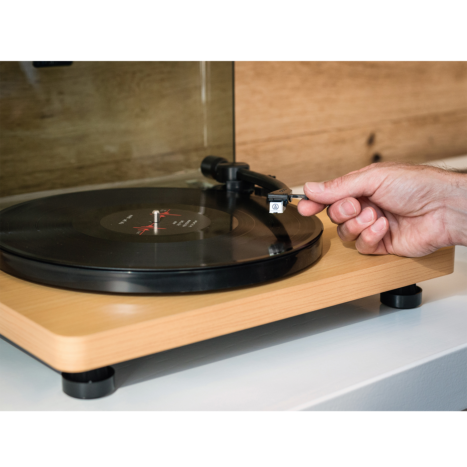 Una mano che tiene uno stilo sopra un disco in vinile su un giradischi in legno.