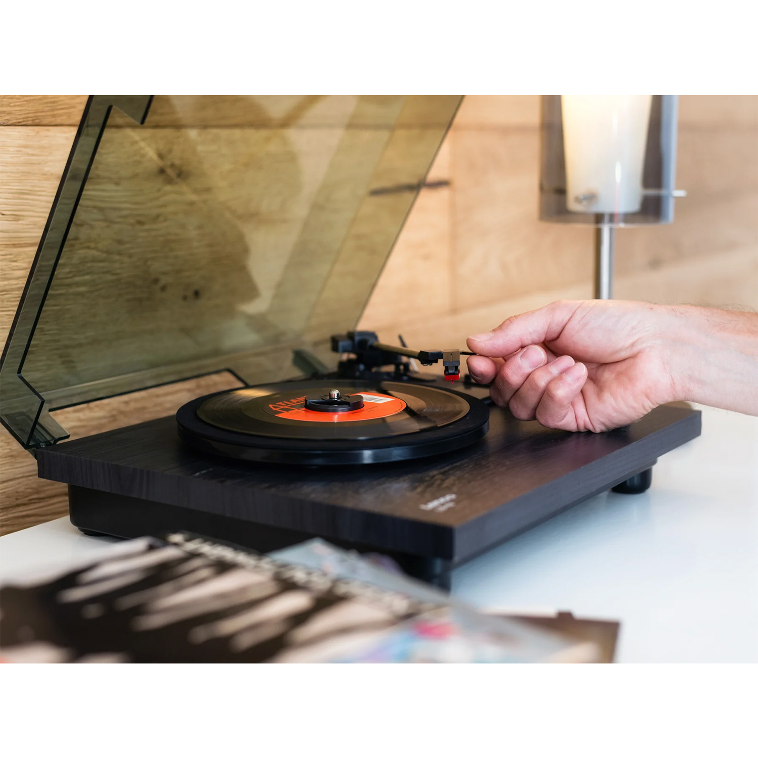 Un giradischi con disco nero in riproduzione, mano che posiziona la puntina. Sfondo in legno.