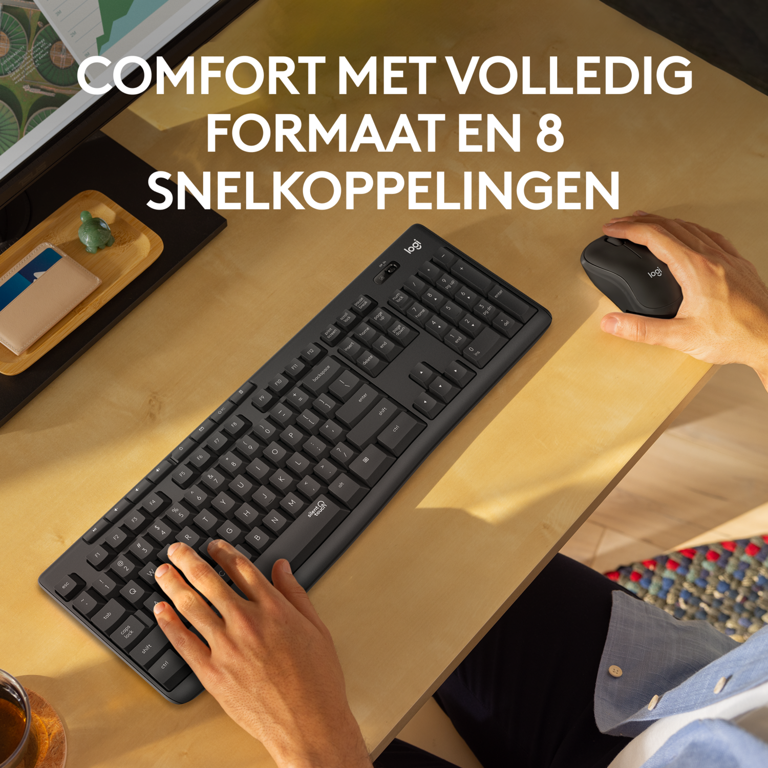 Bovenaanzicht van een zwart toetsenbord, muis en accessoires op een licht houten bureau. Handen zichtbaar.