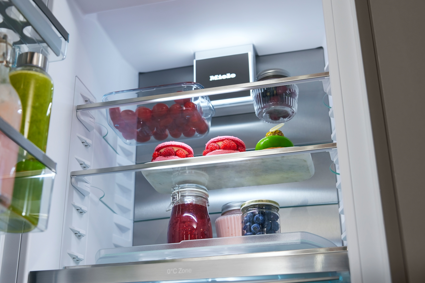 Im Miele Kühlschrank: Gläser mit Obst, Macarons und Desserts auf Ablagen.