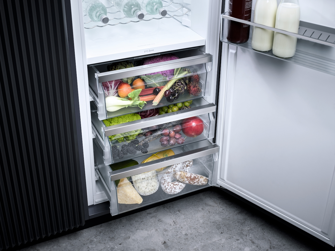 Ein offener Kühlschrank mit mehreren Schubladen voller frischer Lebensmittel wie Obst, Gemüse, Käse und Wurst.