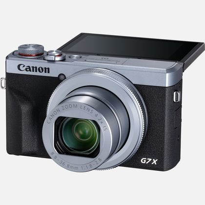 Canon G7X Kamera. Silbernes und schwarzes Gehäuse. Geöffneter Bildschirm, Objektiv sichtbar.