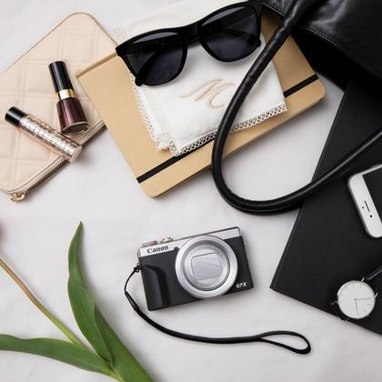 Draufsicht auf Kamera, Tasche, Sonnenbrille, Accessoires auf weißer Fläche.