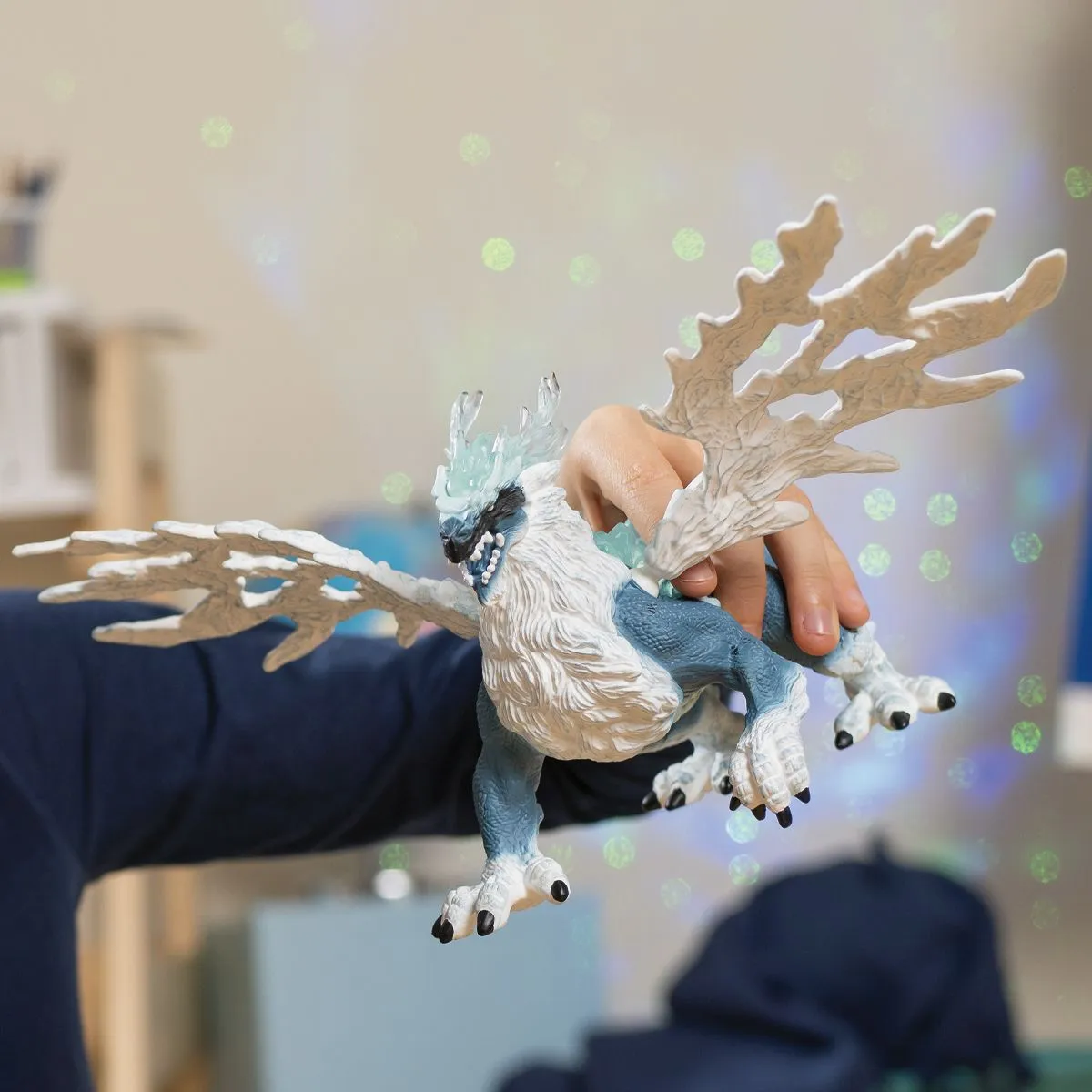 Eine Person hält eine blau-weiße, geflügelte, mythische Kreatur mit einer Hand.