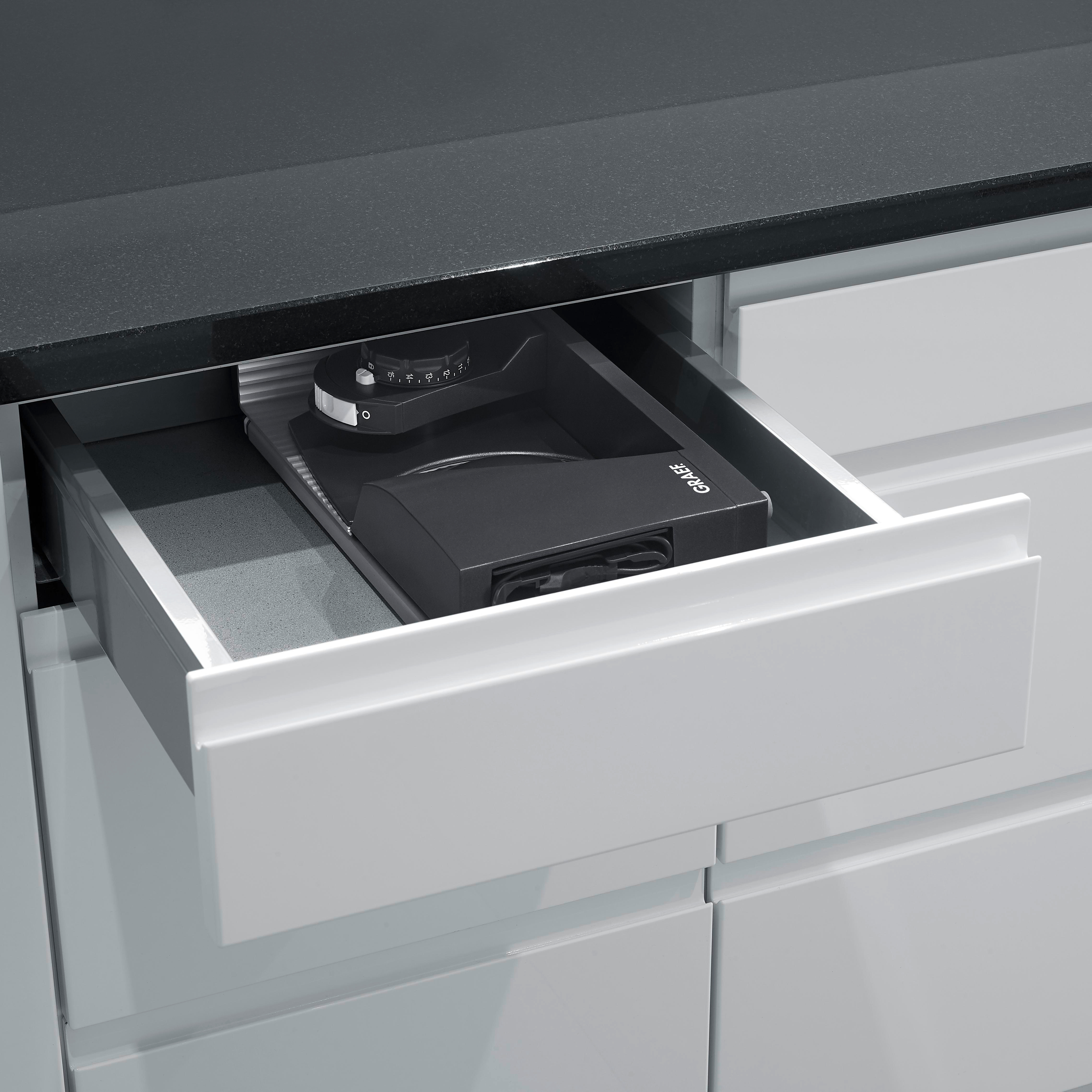 Schublade mit schwarzem Gerät in einem grauen Küchenschrank.