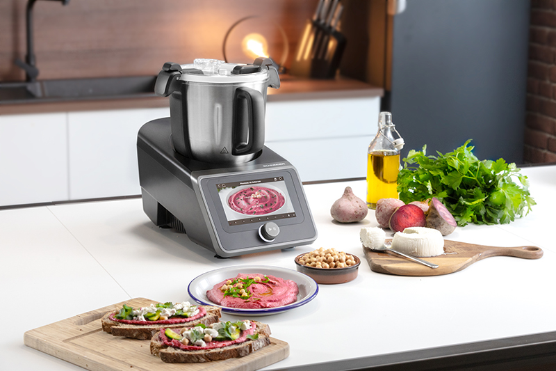 Küchentheke mit Küchenmaschine, Essen und Zutaten auf weißer Oberfläche.
