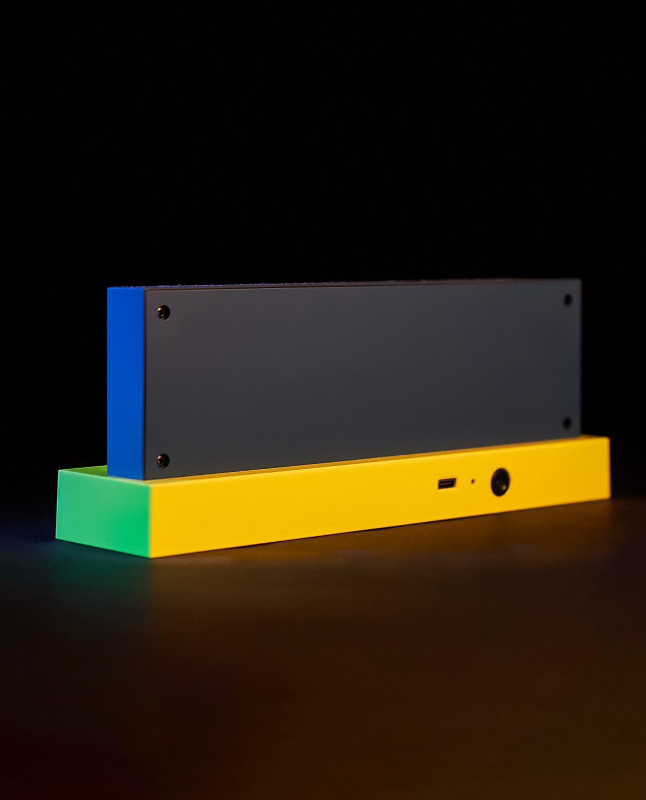 Rechteckiges Gerät, oben blau, Basis gelb. Das Gerät steht auf dunkler, reflektierender Oberfläche.