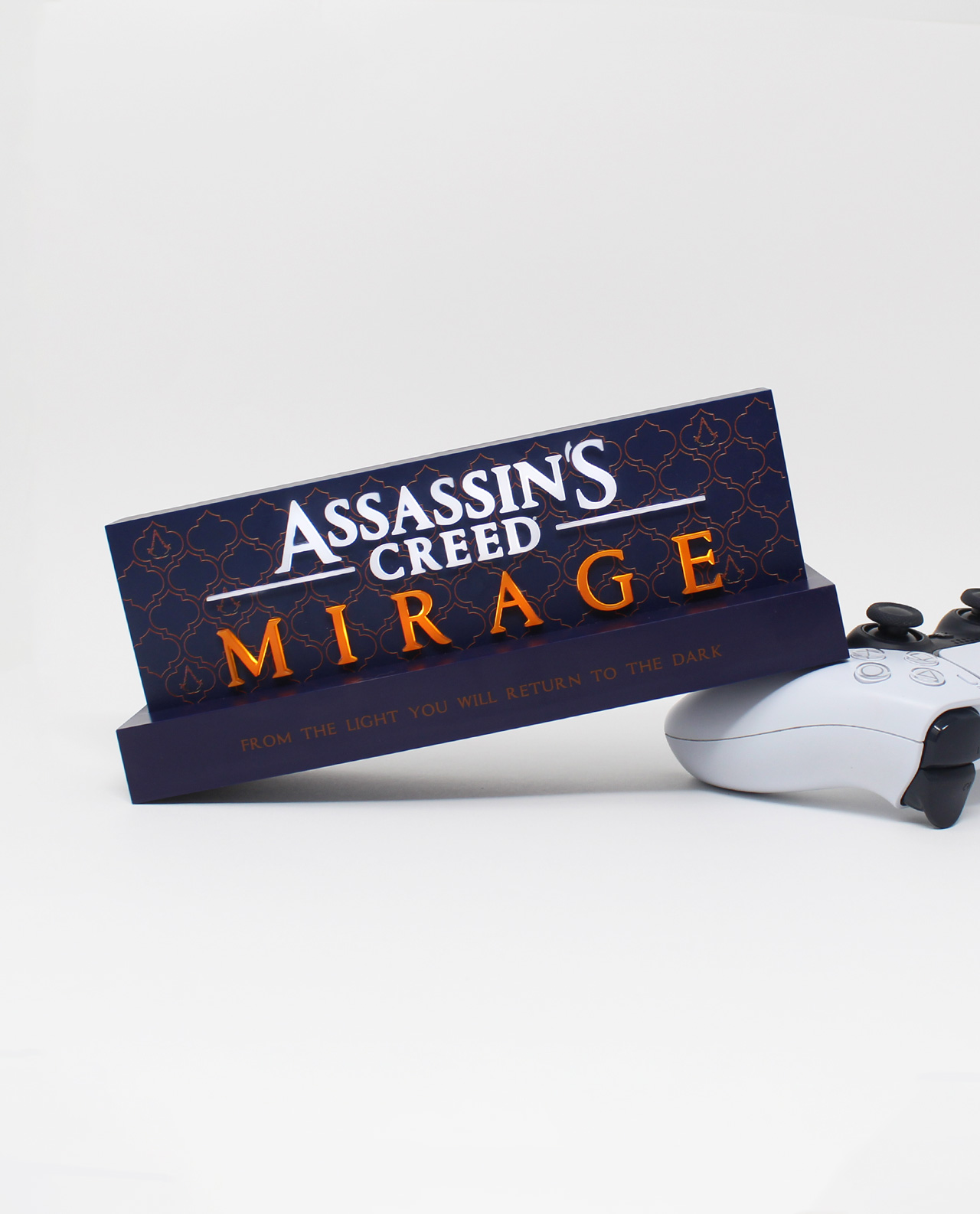 Die Spielbox von Assassin's Creed Mirage liegt auf einer ebenen Fläche mit einem weißen Playstation-Controller.