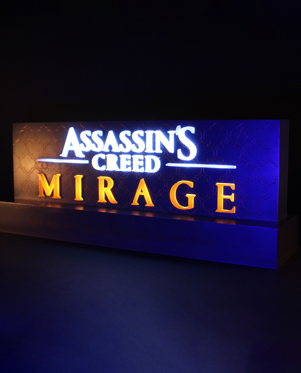 Beleuchtetes Assassin's Creed Mirage-Schild. Weiße und orangefarbene Buchstaben, blauer Hintergrund.